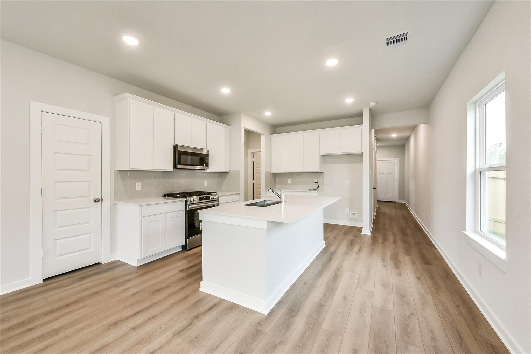 Modern white kitchen with large island, stainless appliances, open layout in The Frio G floor plan, Dayton, Texas