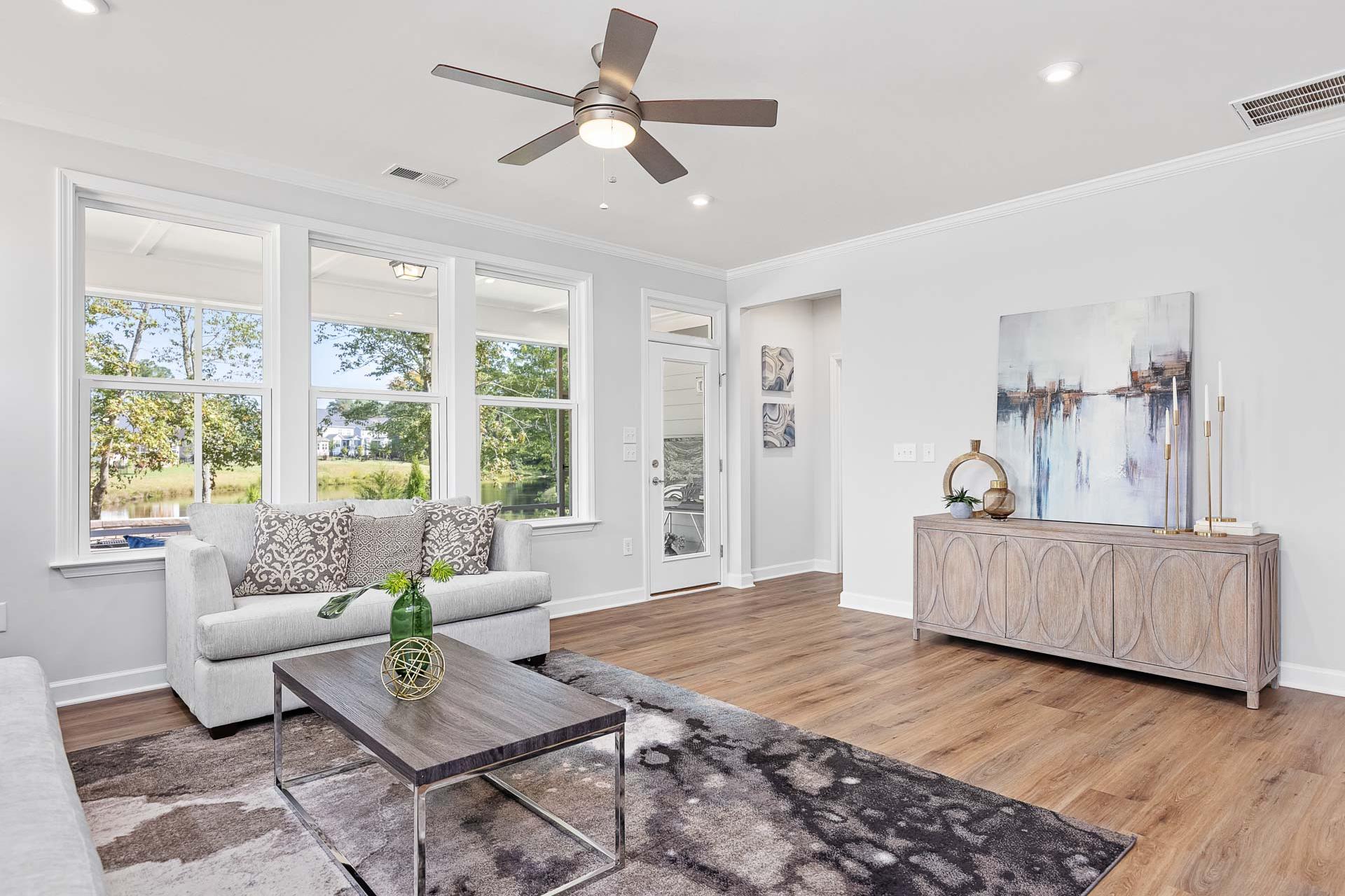 Spacious living room at Glenmere in Knightdale NC with large windows, neutral sofa, abstract art, hardwood floors by Davidson Homes
