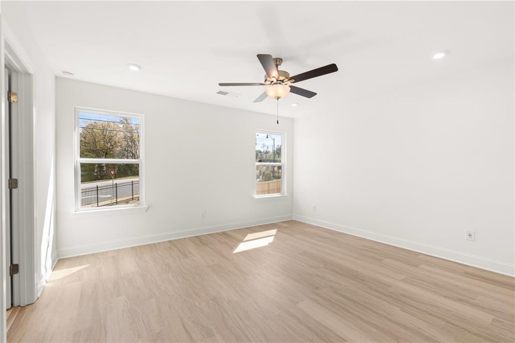 Bright bedroom with light wood floors, large windows overlooking trees, and ceiling fan in Davidson Homes The Gavin E, Kennesaw, GA