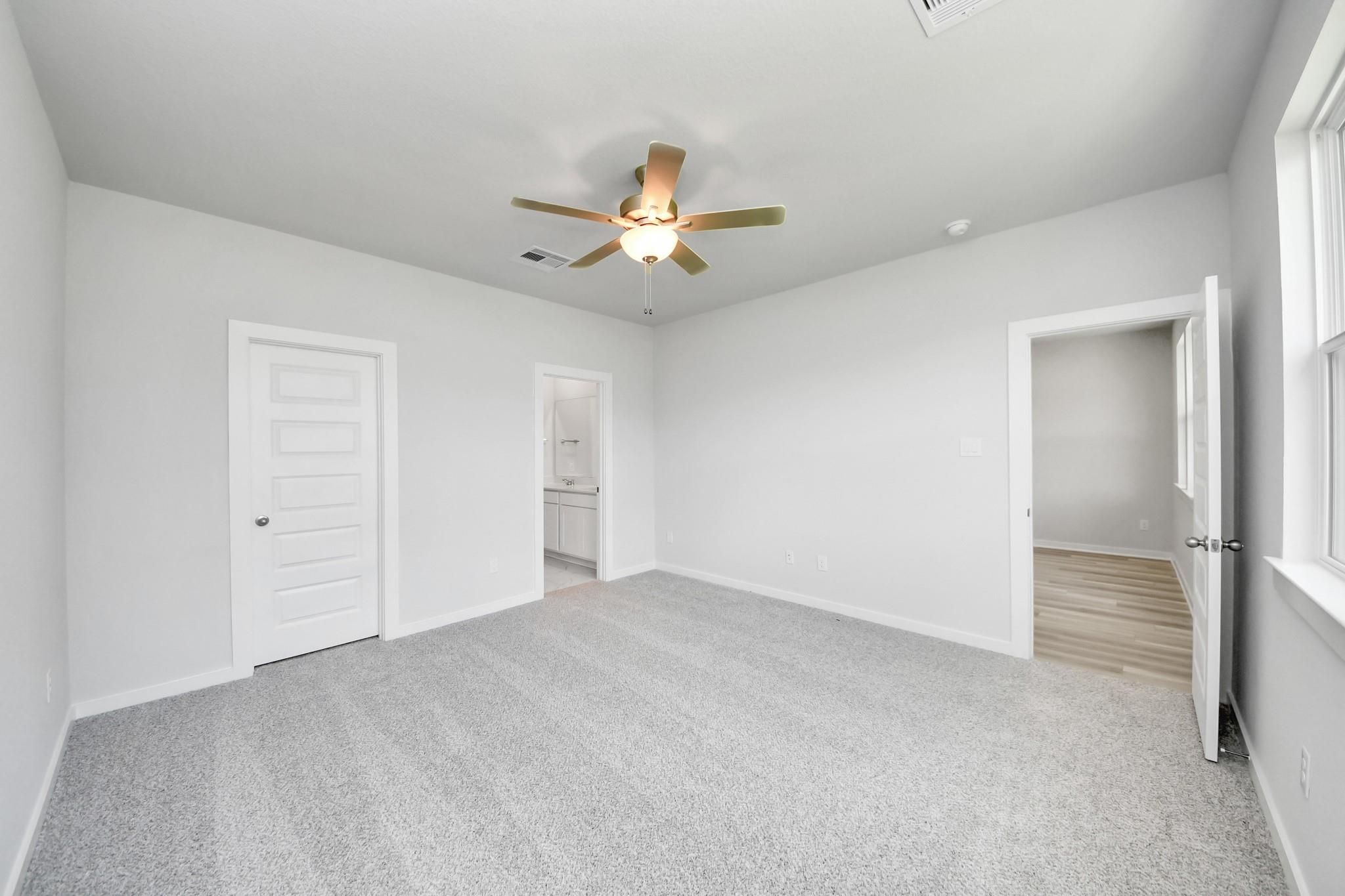 Spacious bedroom with grey carpet and ceiling fan in The Sabine F floor plan at Liberty Estates, Cleveland, Texas.