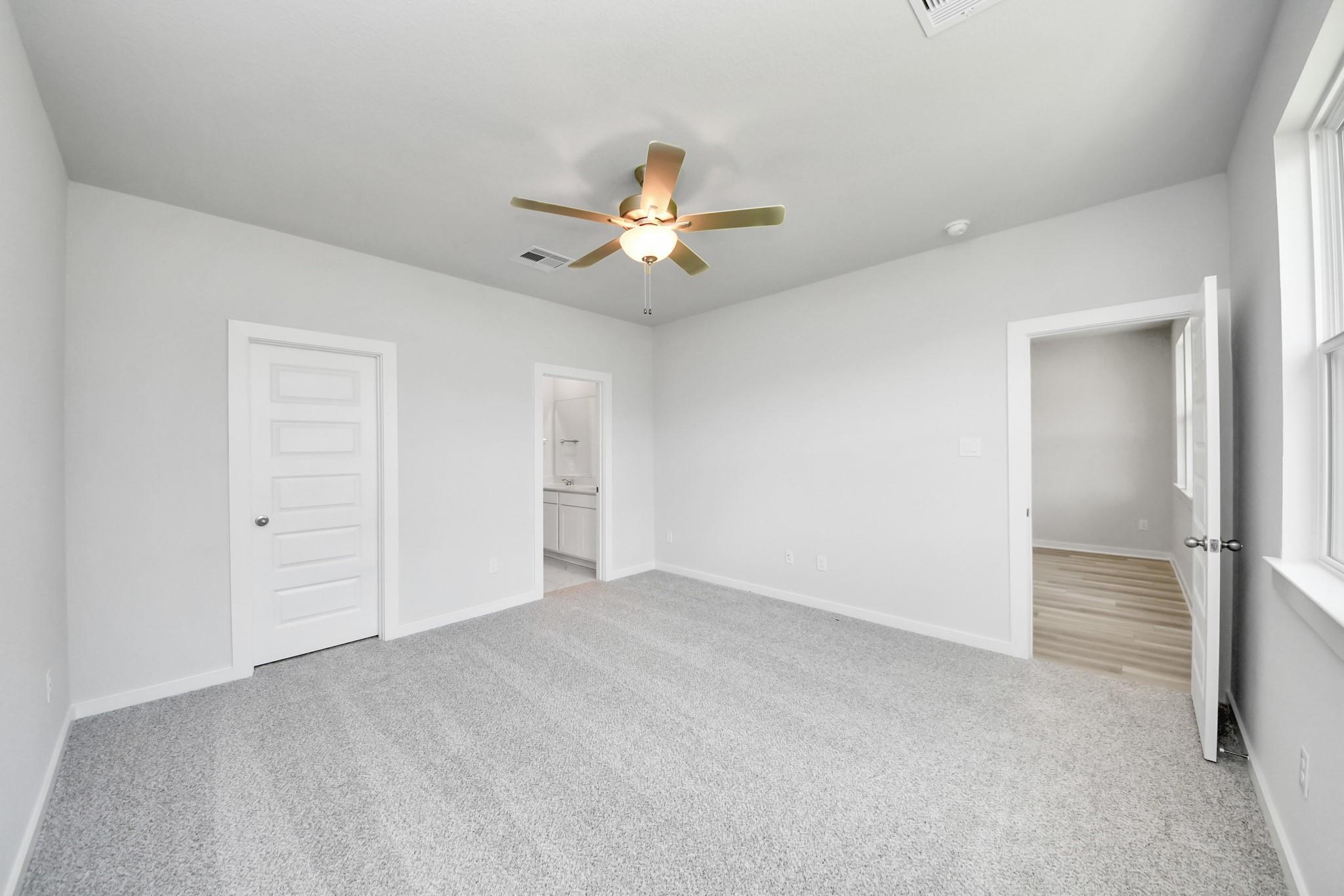 Spacious bedroom with grey carpet and ceiling fan in The Sabine F floor plan at Liberty Estates, Cleveland, Texas.