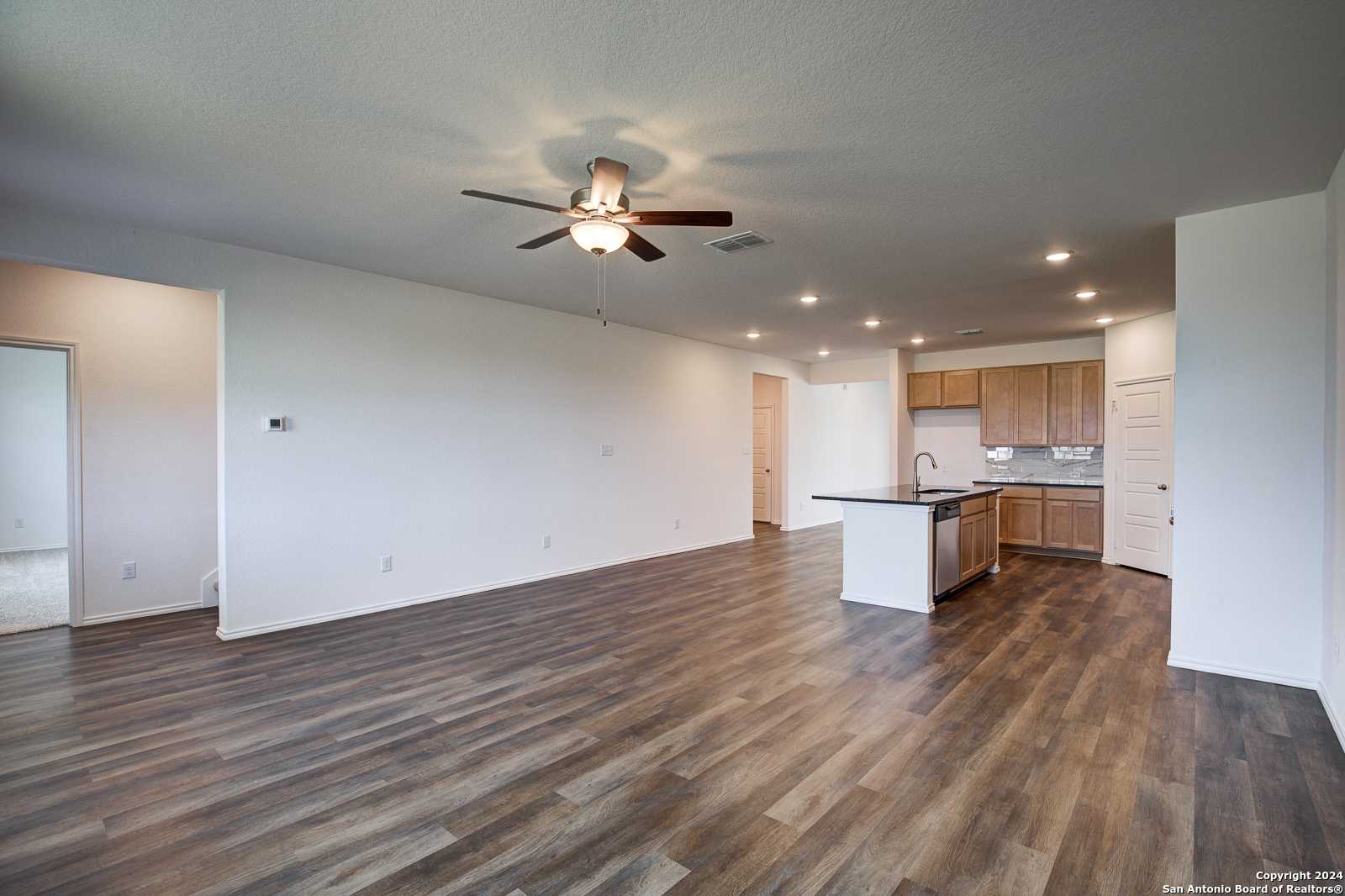 Open kitchen with oak cabinets, dark granite island sink, ceiling fan, and luxury vinyl plank floors in Davidson Homes Douglas D, Seguin, TX