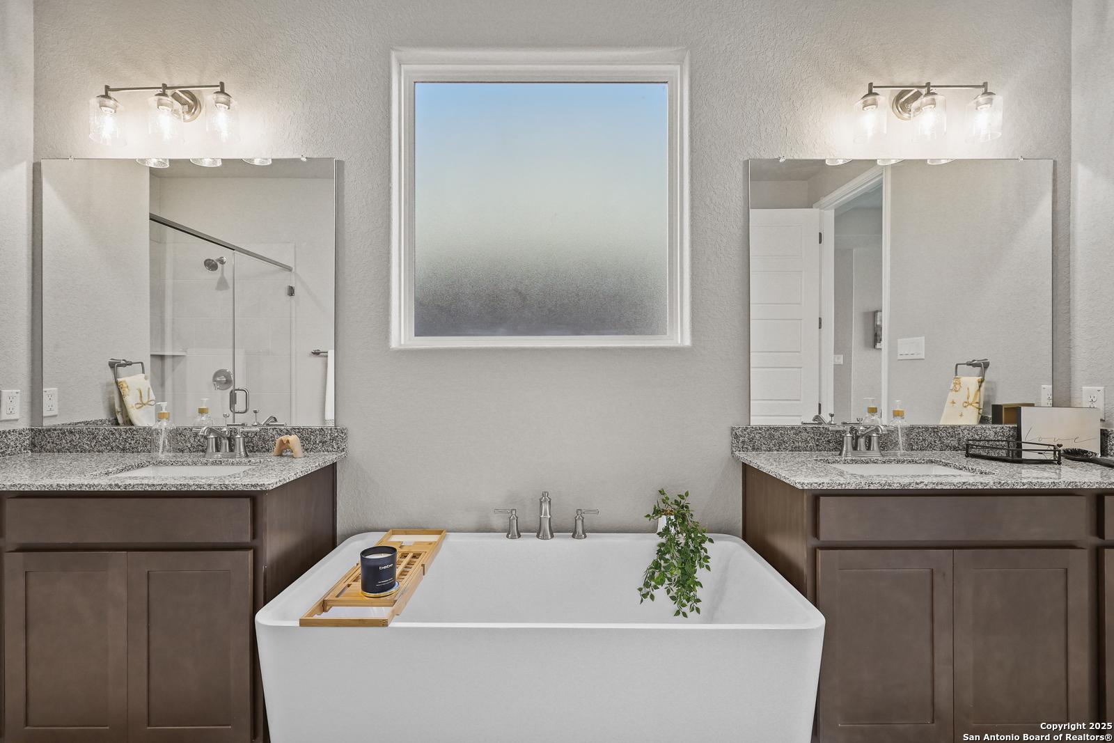 Elegant master bath with freestanding tub, double vanity, mirrors, and frosted window in Davidson Homes The Jennings G, Castroville, TX