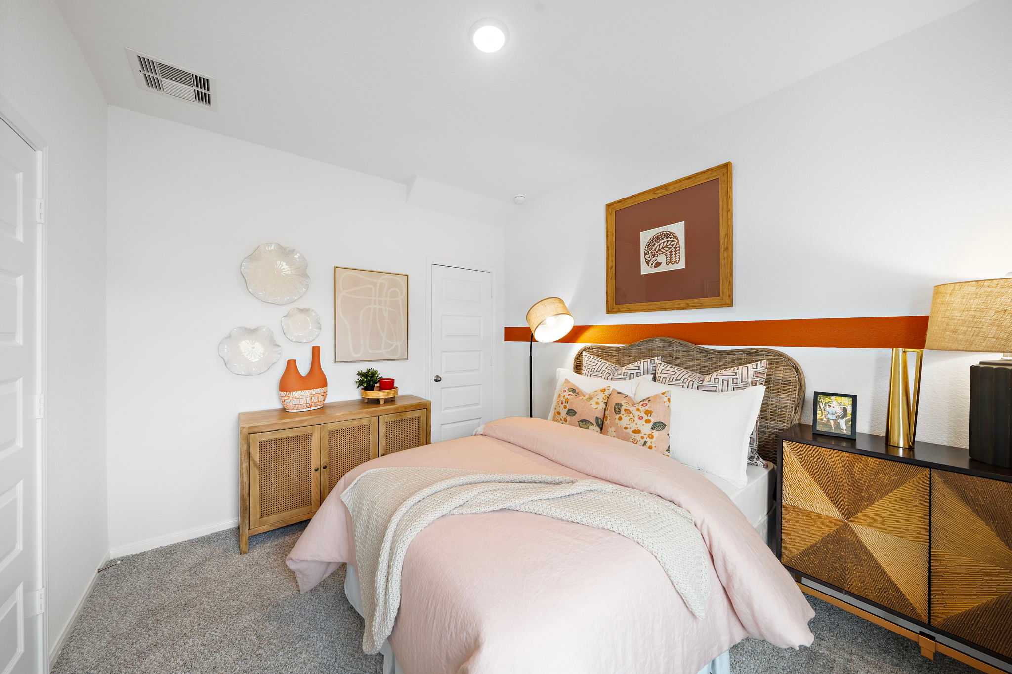 Cozy bedroom interior at The Villages at WestPointe in Dayton Texas by Davidson Homes with pink duvet, wooden dresser, and wall art