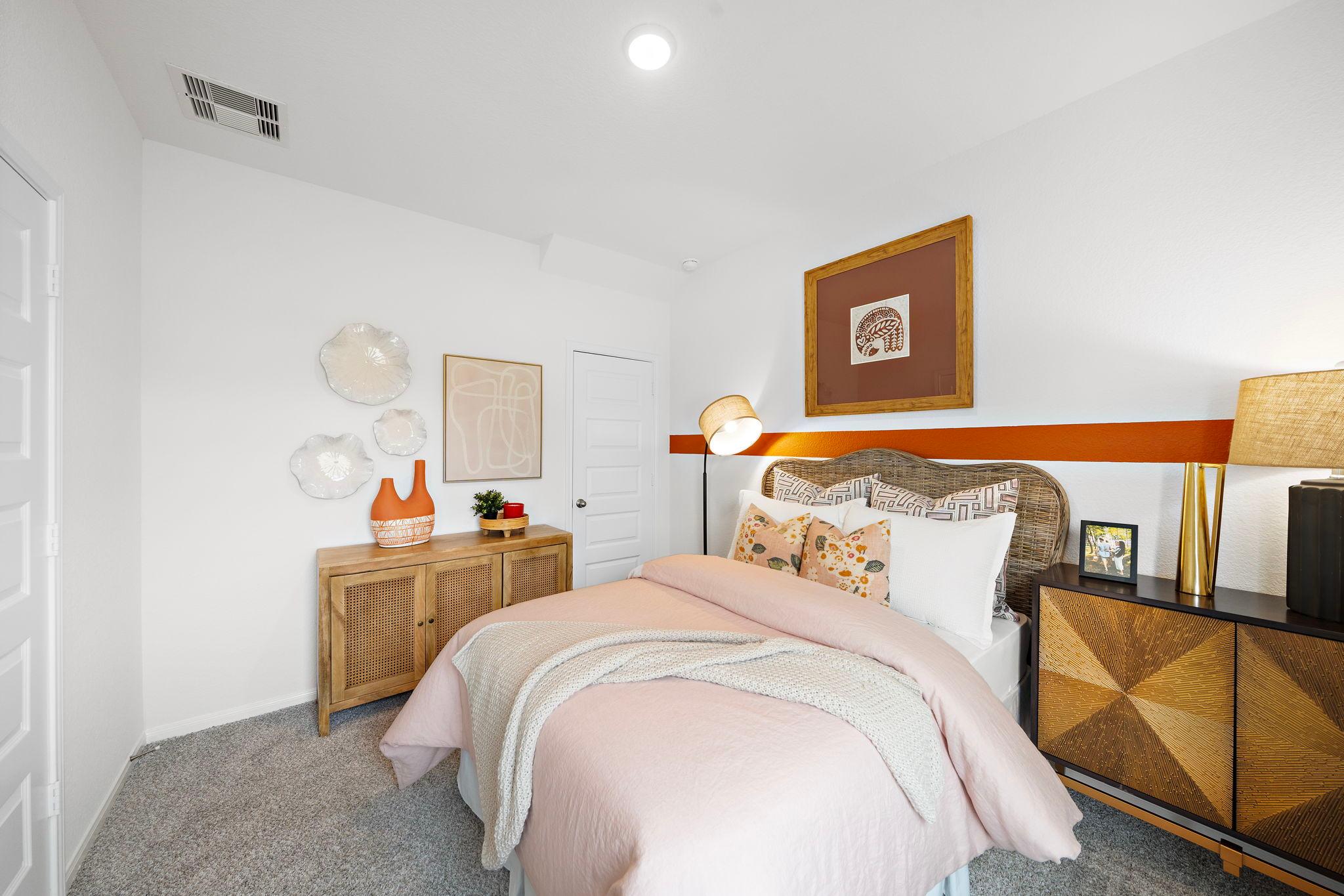 Cozy bedroom interior at The Villages at WestPointe in Dayton Texas by Davidson Homes with pink duvet, wooden dresser, and wall art