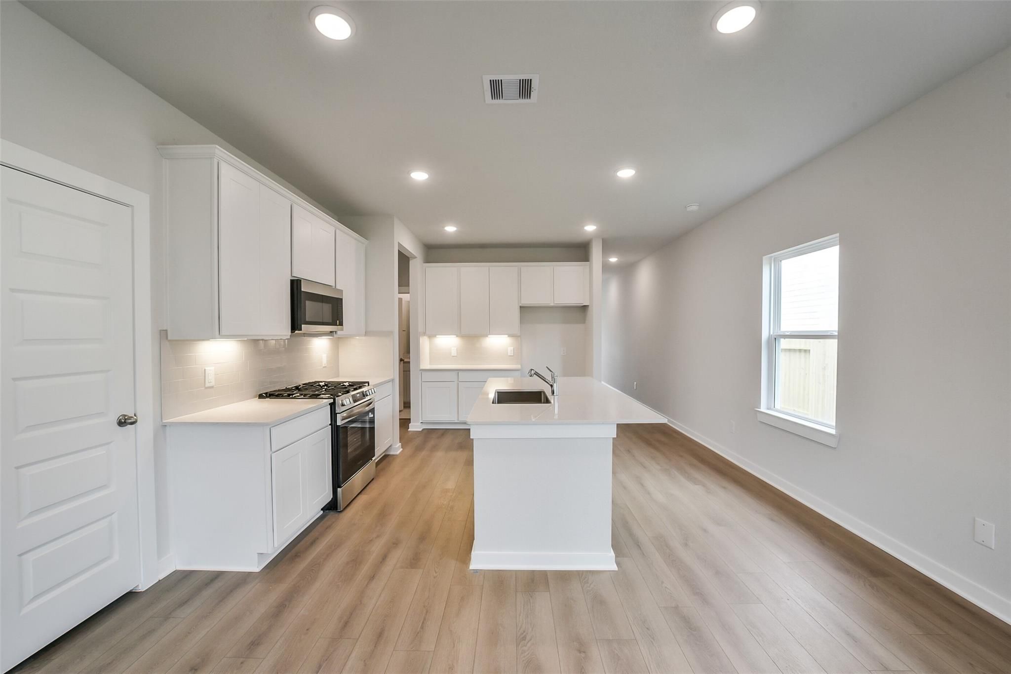 Modern white kitchen with large island, stainless steel appliances, and open layout in Davidson Homes The Frio F, Conroe Texas