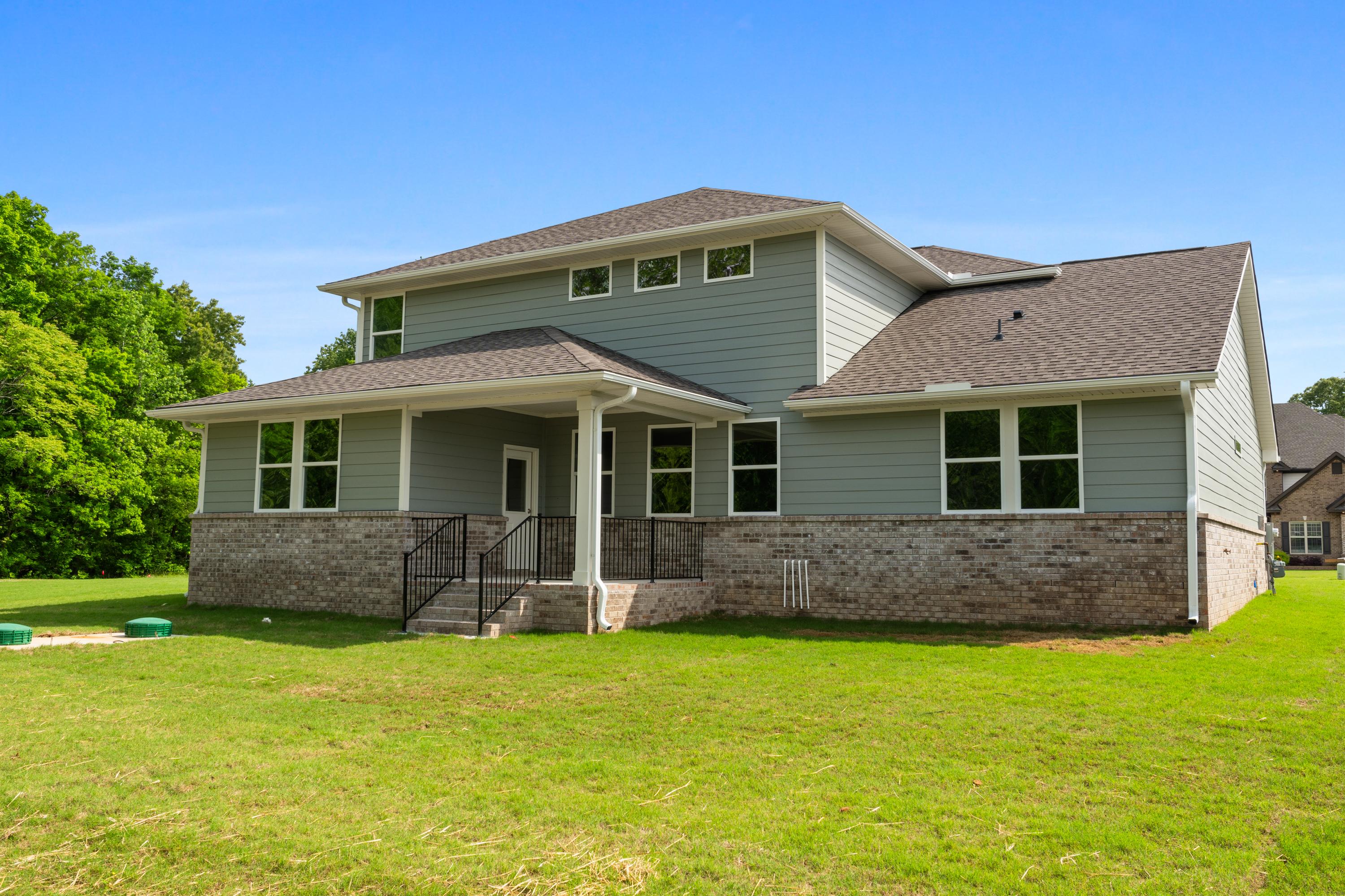 Rear elevation of The Avalon D two-story home featuring gray siding, brick base, covered porch, and lush green backyard in Owens Cross Roads, Alabama
