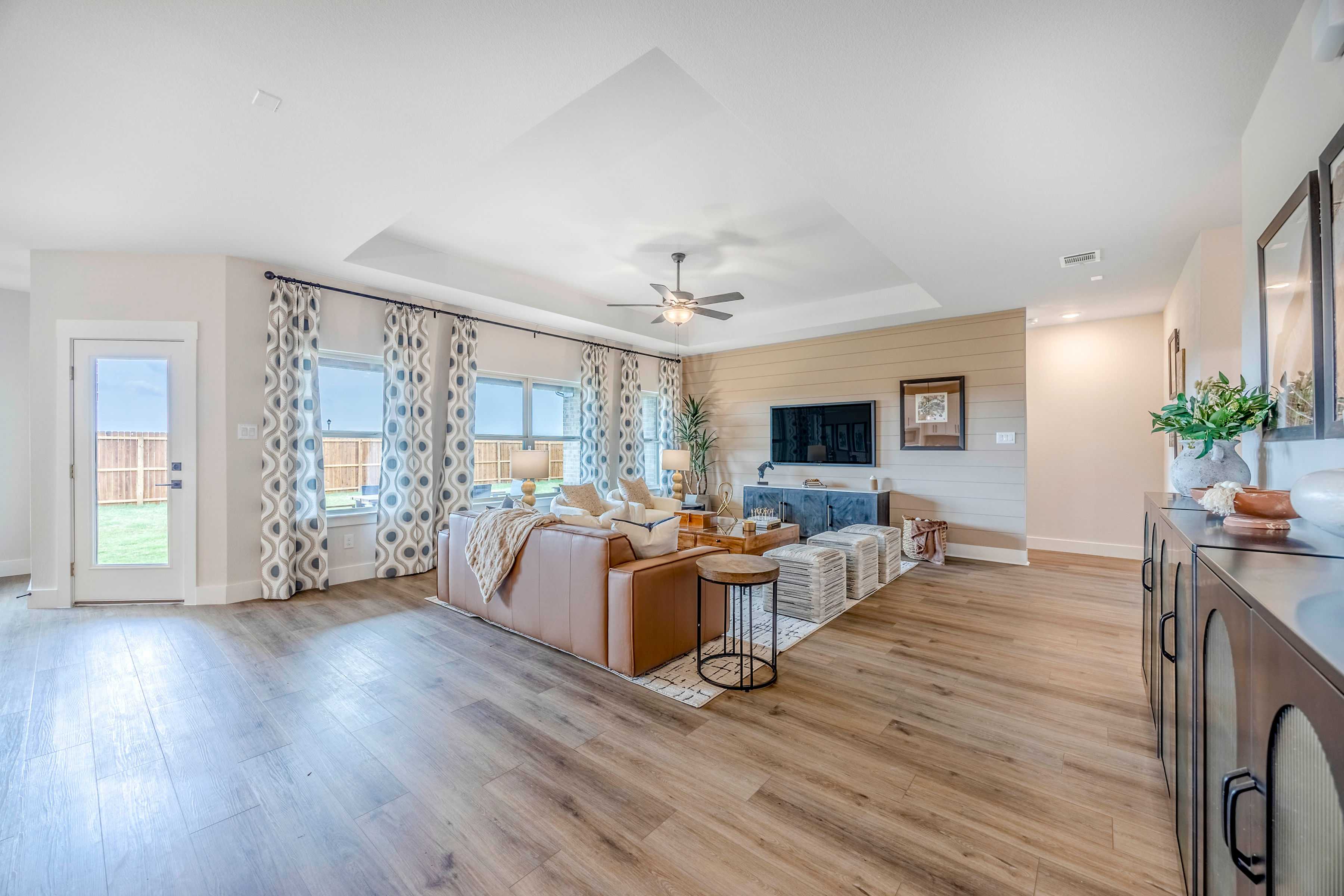 Spacious open-concept living room at Waverly Estates in Josephine Texas with beige leather sectional, hardwood floors, and large curtained windows