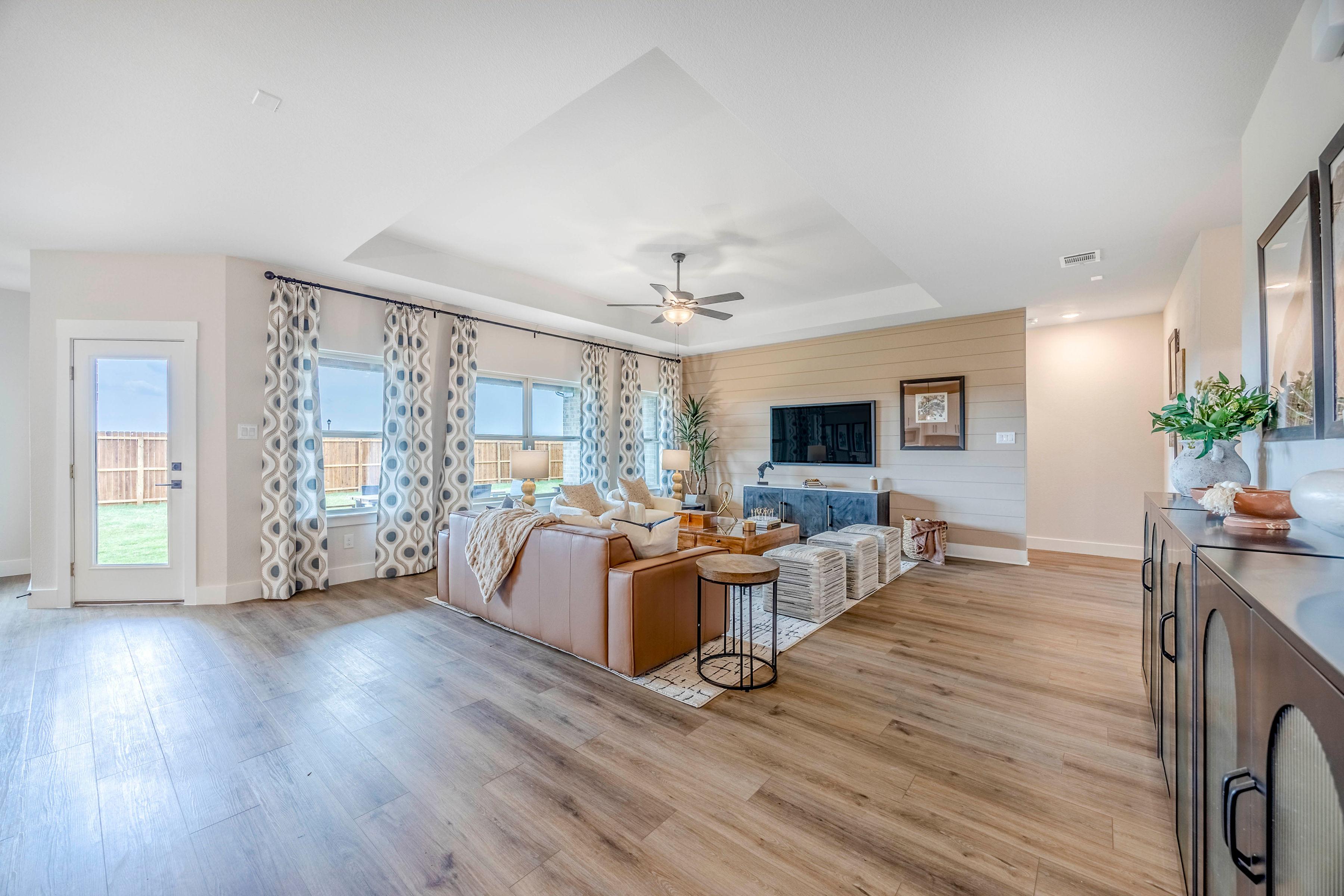 Spacious open-concept living room at Waverly Estates in Josephine Texas with beige leather sectional, hardwood floors, and large curtained windows