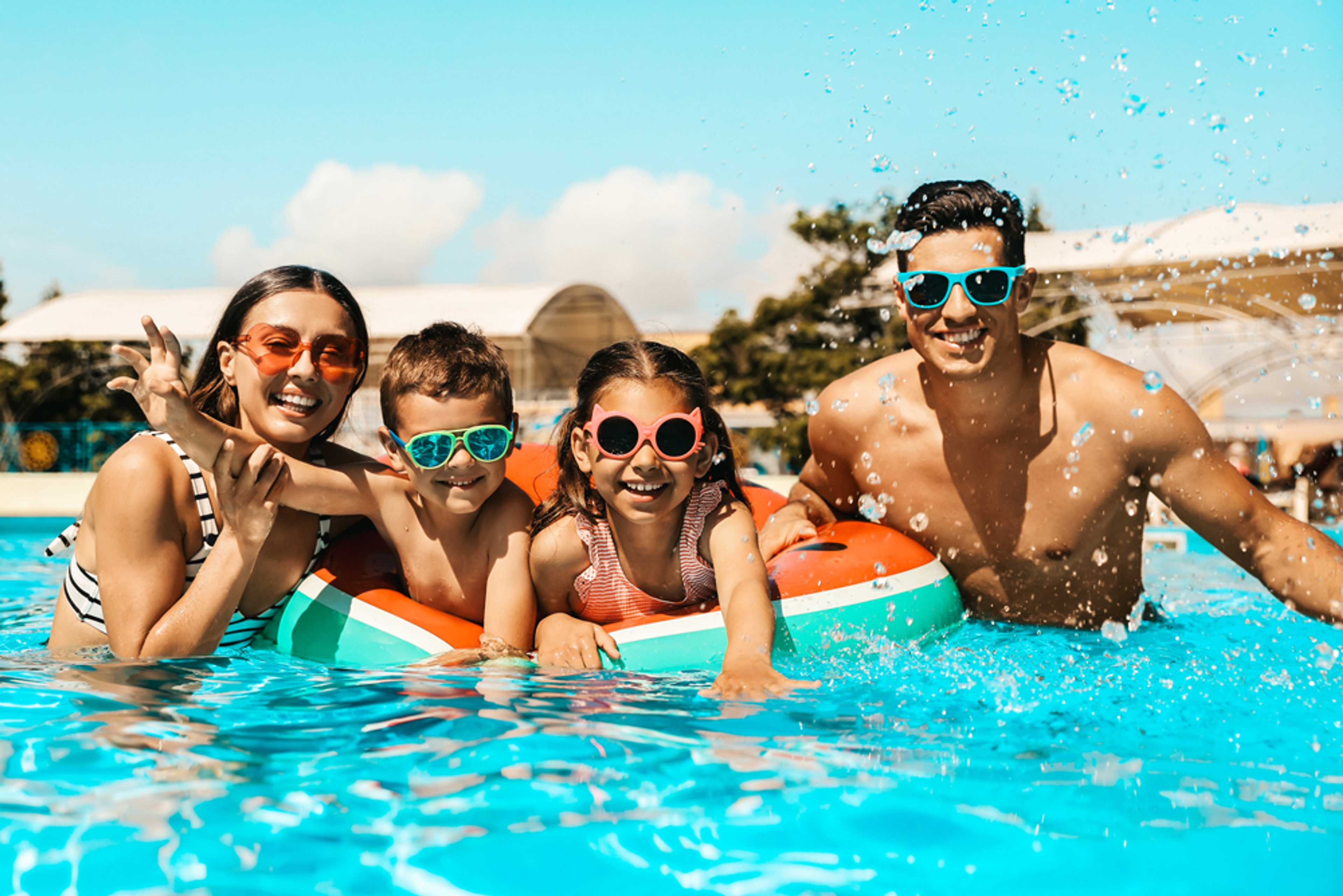 Happy family of four in Emberly community pool, Beasley Texas, splashing with watermelon float and colorful sunglasses