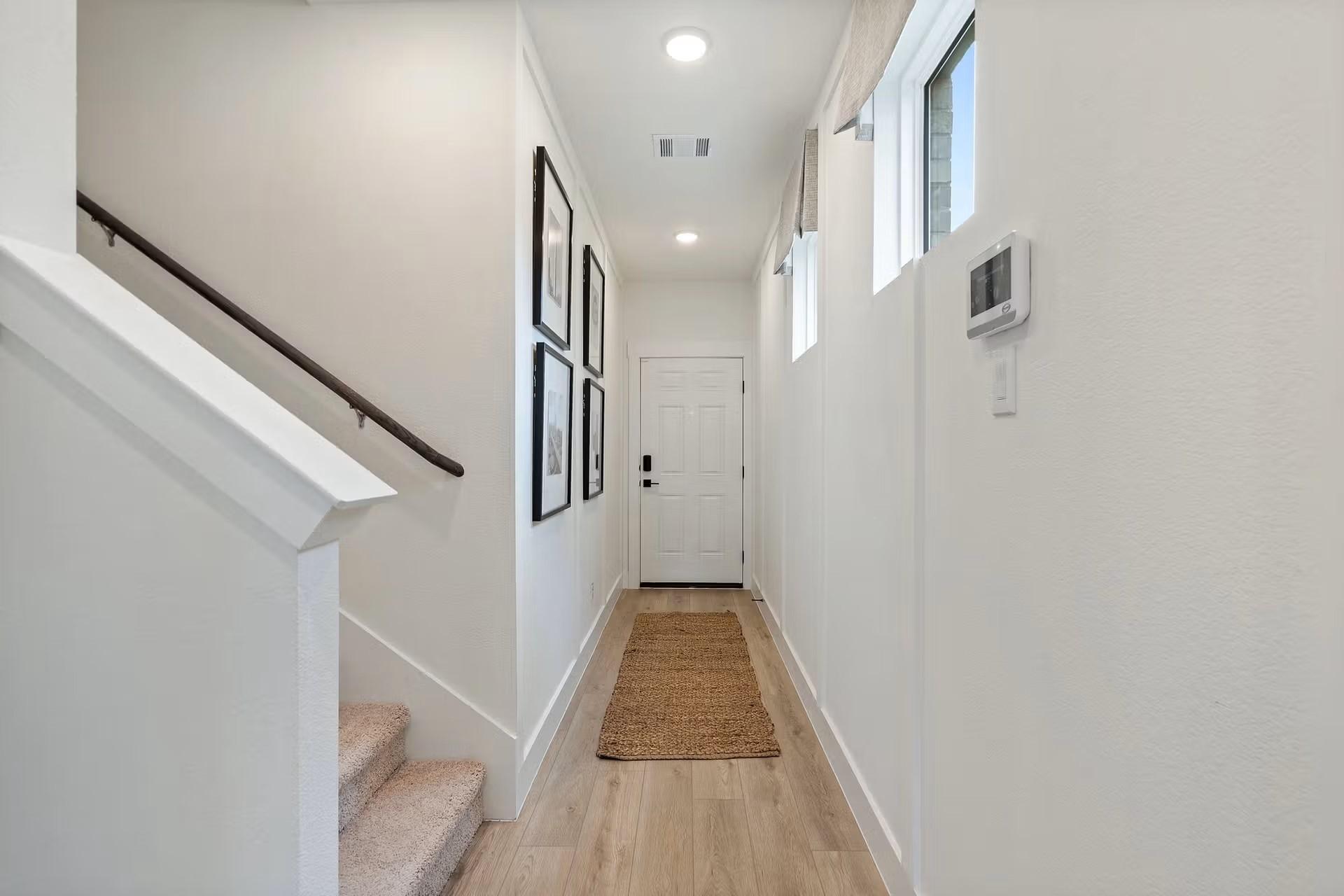 Bright upstairs hallway with white walls, seagrass rug, framed art, and carpeted stairs in Davidson Homes The Wake C, Wylie, Texas
