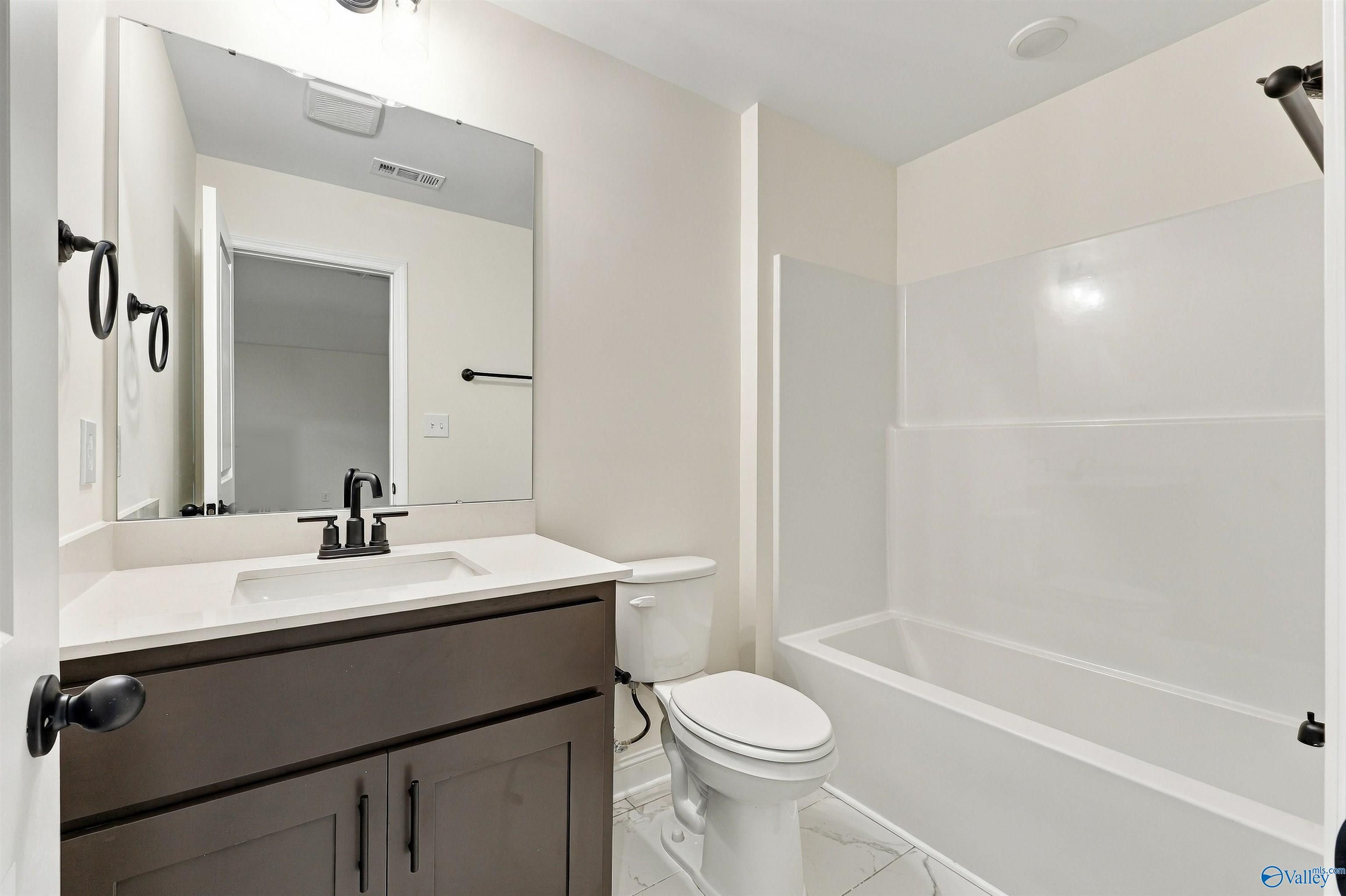 Modern bathroom with dark wood vanity, black fixtures, white tile surround tub, and toilet in Davidson Homes Valencia floor plan, Huntsville