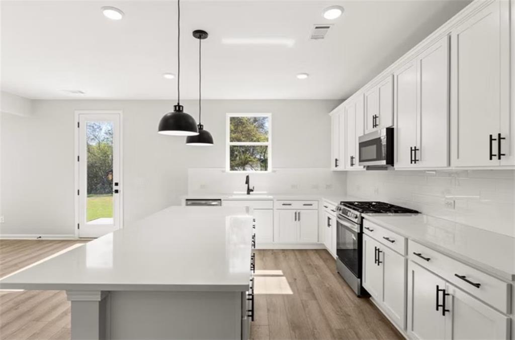 Modern white kitchen with large quartz island, stainless steel appliances, and French doors to backyard in Davidson Homes Hickory B, Winder GA