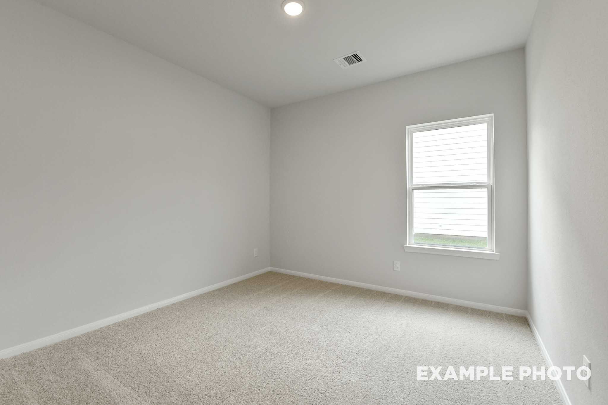 Bright, neutral-toned secondary bedroom in The Frio floor plan by Davidson Homes featuring plush carpeting and a window.