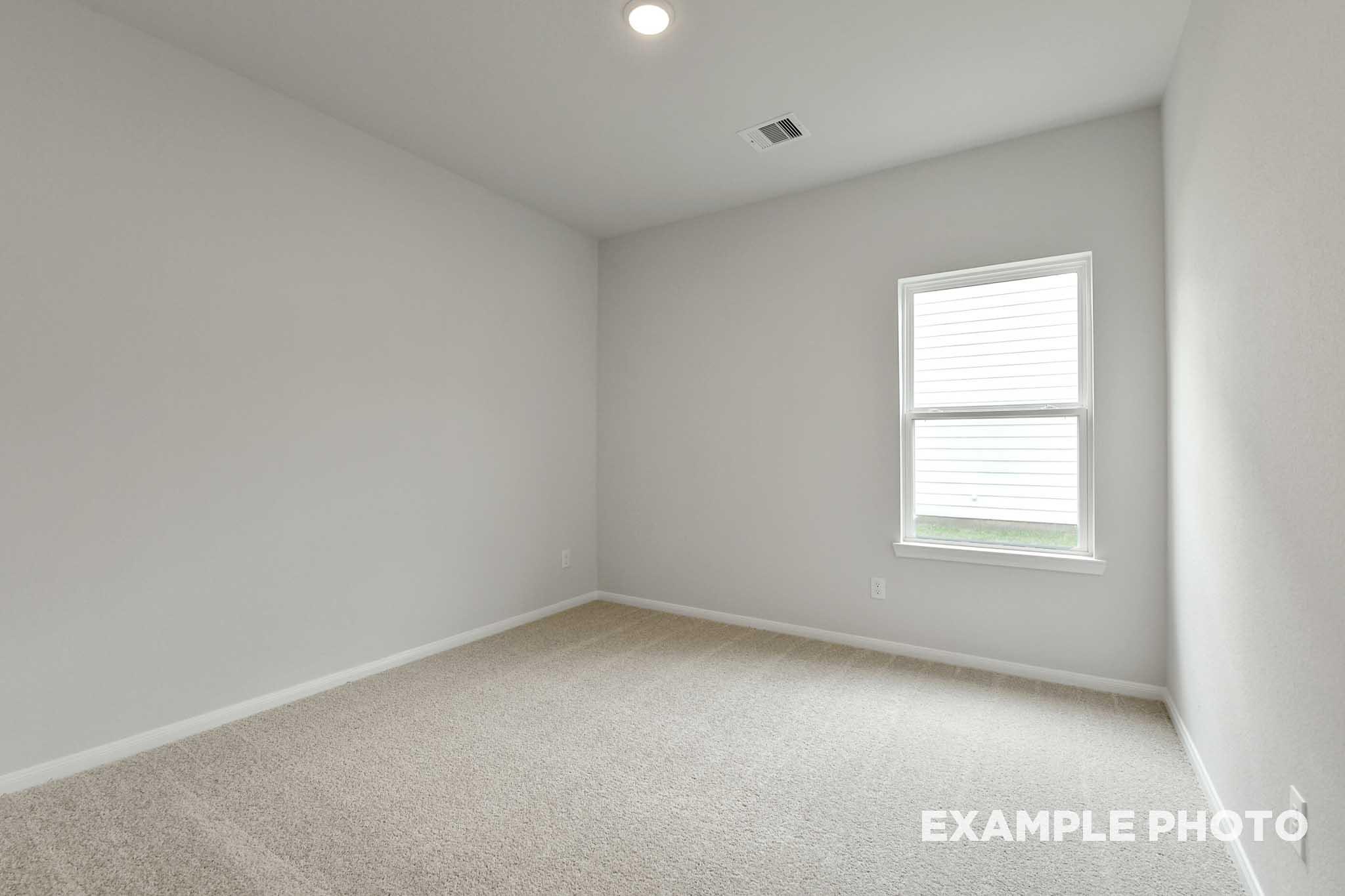 Bright, neutral-toned secondary bedroom in The Frio floor plan by Davidson Homes featuring plush carpeting and a window.