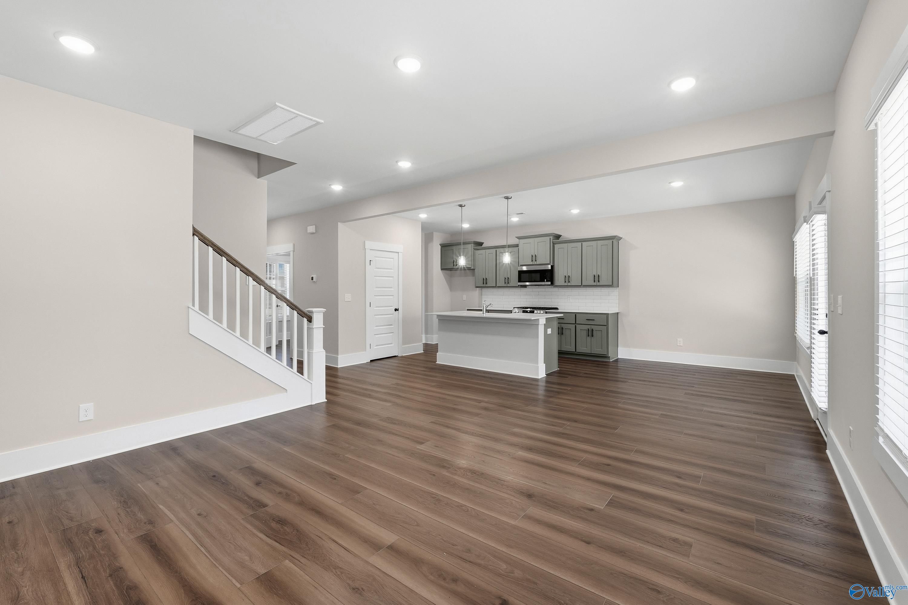 Open-concept living kitchen with hardwood floors, gray cabinets, island, and staircase in Davidson Homes Shelby A, Athens AL
