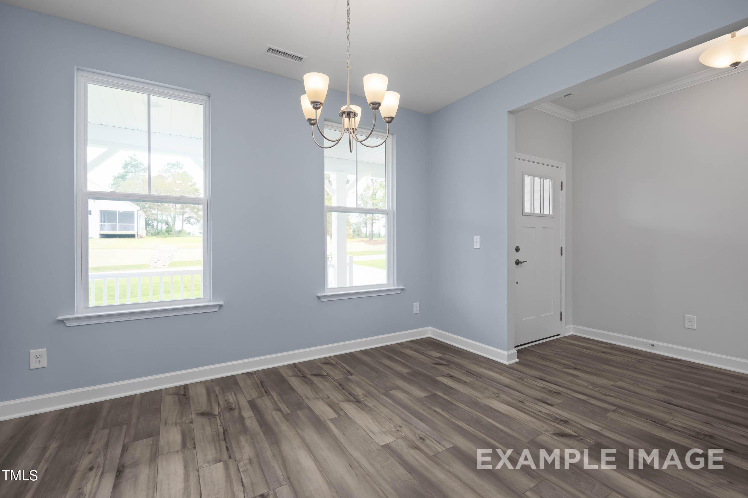 Elegant living room with light blue walls, hardwood floors, chandelier, and large windows in Davidson Homes The Willow E, Angier NC