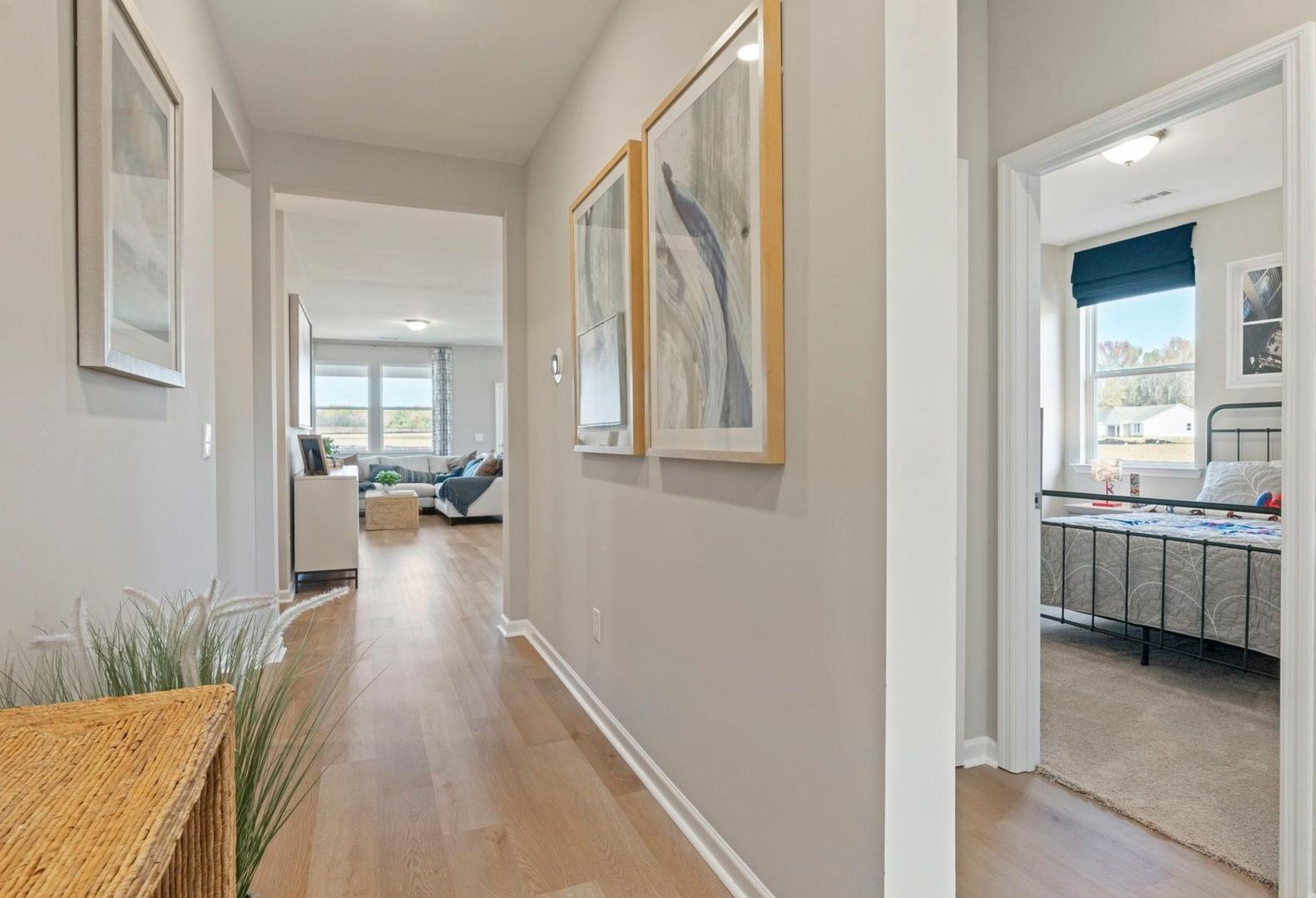 Spacious hallway in The Phoenix A home with hardwood floors, coastal art, potted grass, open living room, and adjacent bedroom with blue bedding