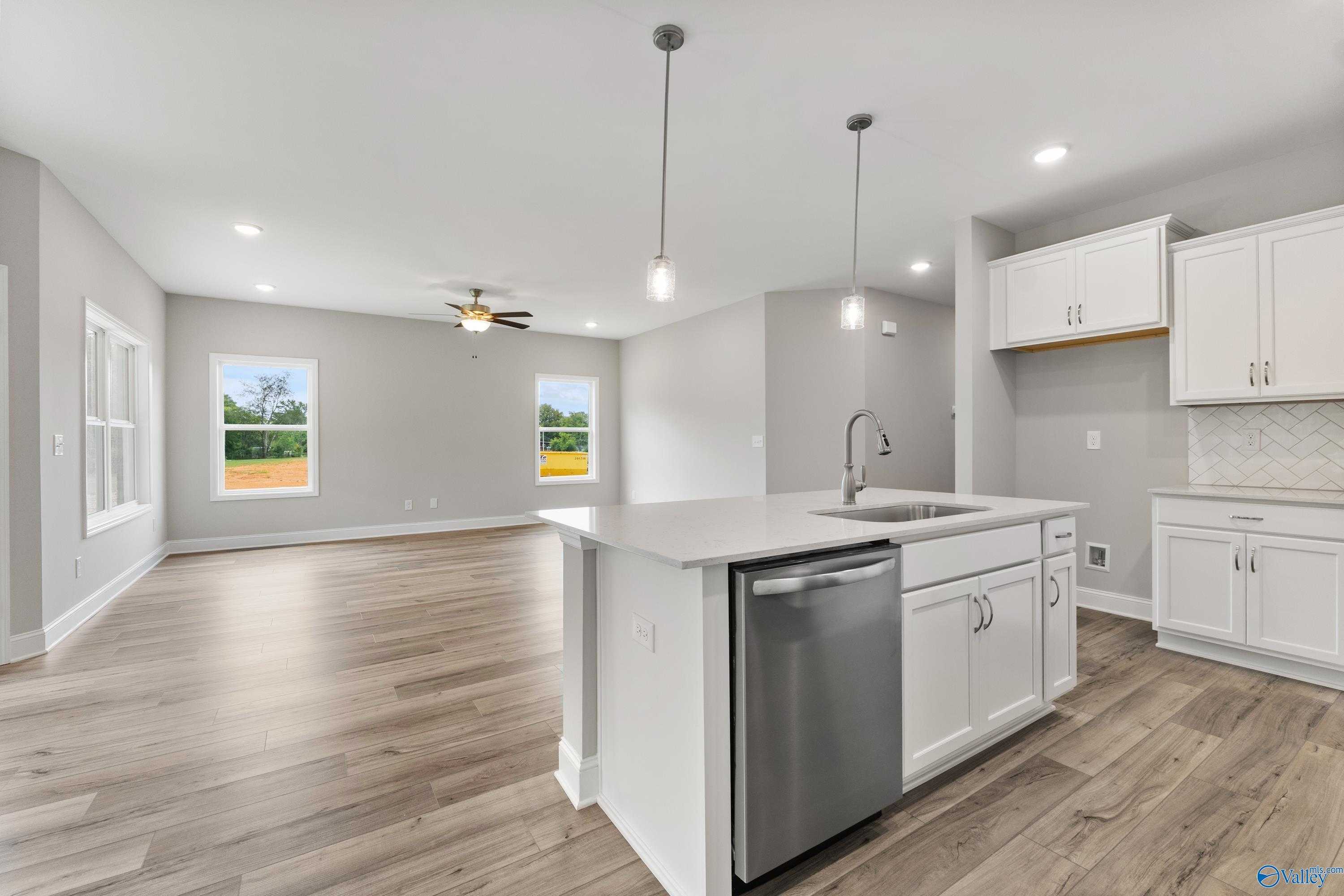 Open-concept kitchen with white cabinets, center island sink, stainless dishwasher, and large windows in The Franklin home by Davidson Homes, Huntsville AL