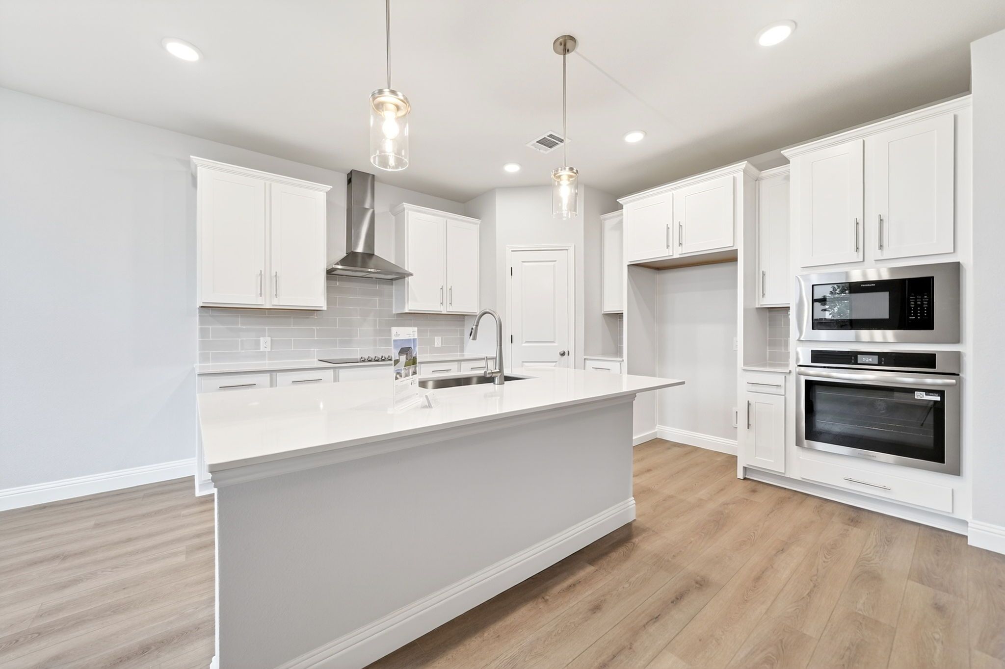 Modern kitchen in The Redbud design featuring white cabinetry, quartz countertops, large island, and stainless appliances.
