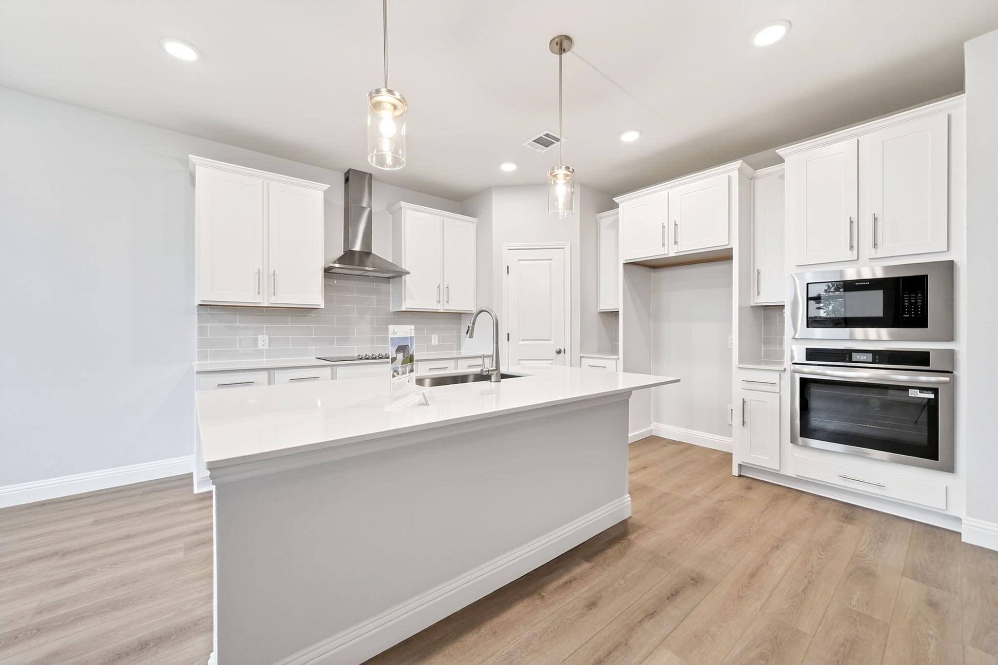 Modern kitchen in The Redbud design featuring white cabinetry, quartz countertops, large island, and stainless appliances.