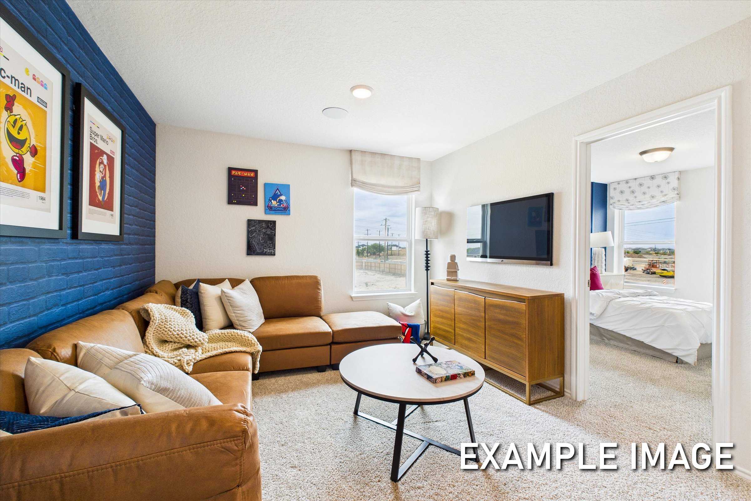 Cozy upstairs media room in The Brazos A featuring blue accent wall, leather sectional sofa, mounted TV, and bedroom glimpse