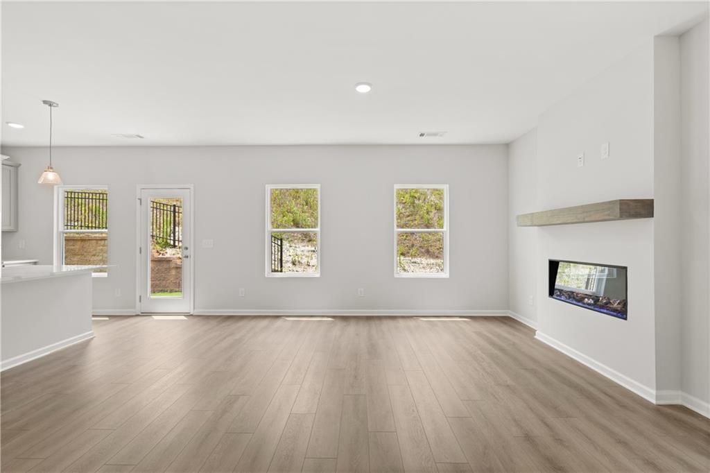 Open-concept living room with modern fireplace and wood-style flooring in The Burton A home, The Bluffs, Canton, GA.