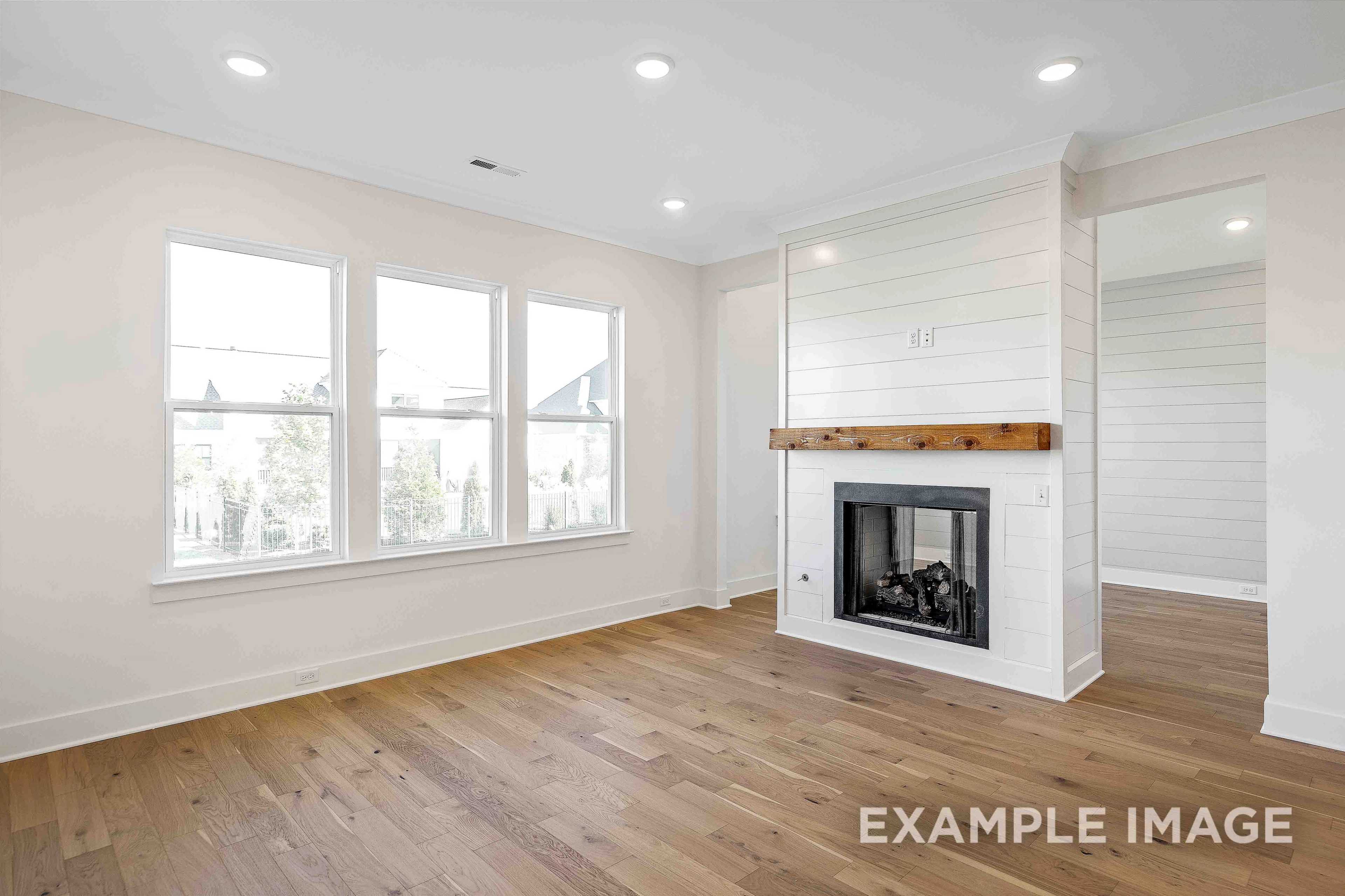 Spacious great room in The Albany A Davidson Homes with shiplap fireplace wall, hardwood floors, and large triple windows