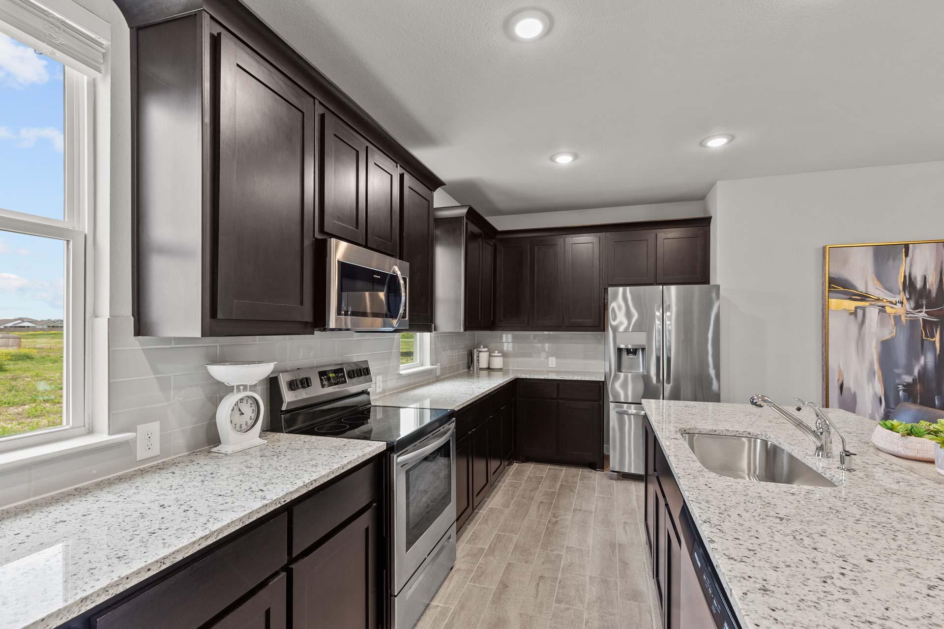Modern kitchen in The Collin A by Davidson Homes with dark cabinets, white quartz counters, stainless appliances, subway tile backsplash