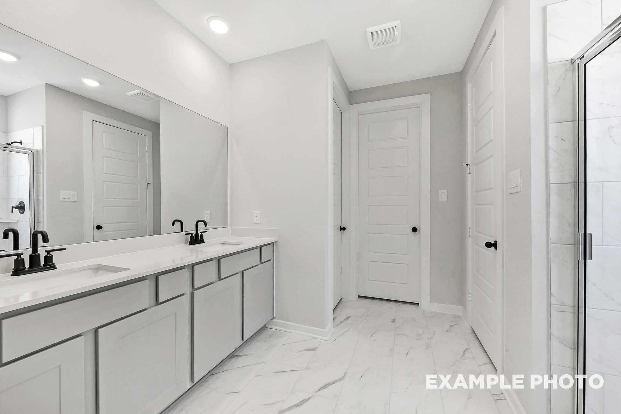 Spacious master bathroom in The Sequoia featuring double vanity sinks, frameless glass shower, and neutral gray tones