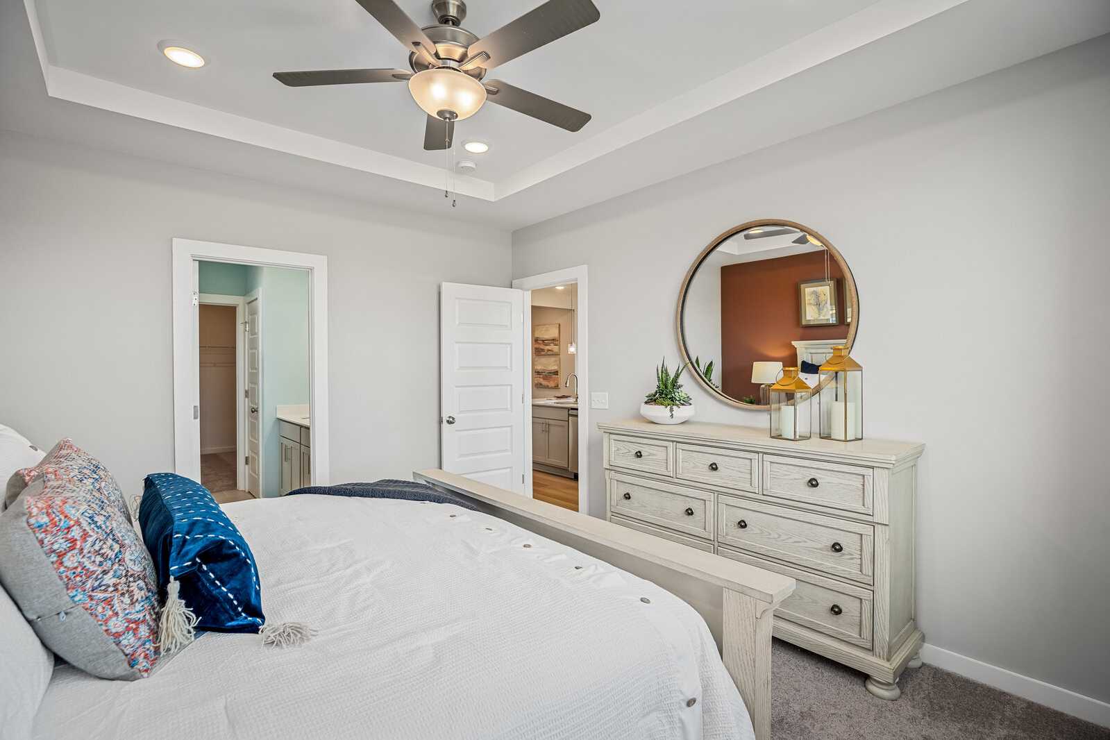 Spacious primary bedroom at Sage Farms in White House TN with gray walls, ceiling fan, king bed, antique dresser, and en-suite bath