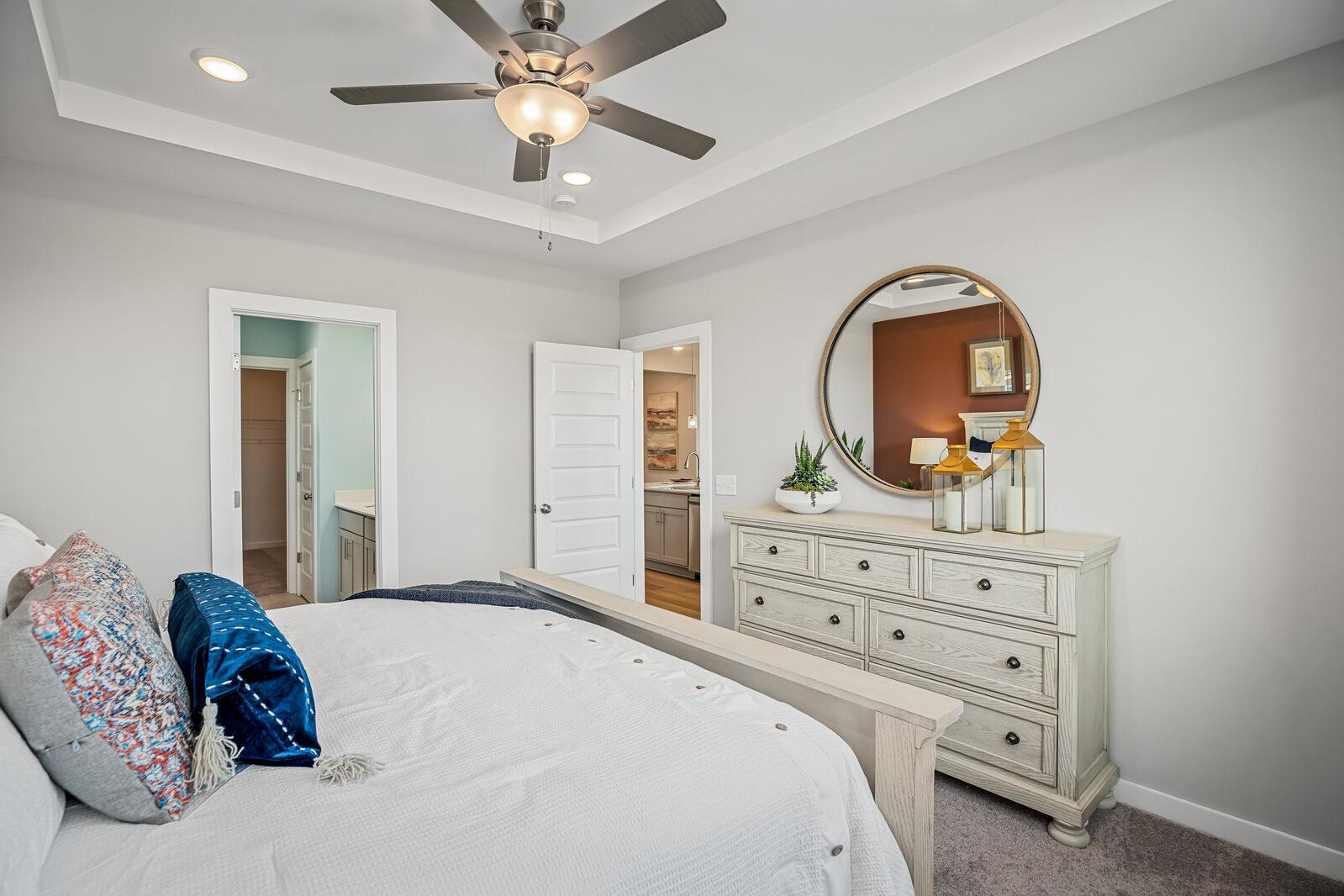 Spacious primary bedroom at Sage Farms in White House TN with gray walls, ceiling fan, king bed, antique dresser, and en-suite bath