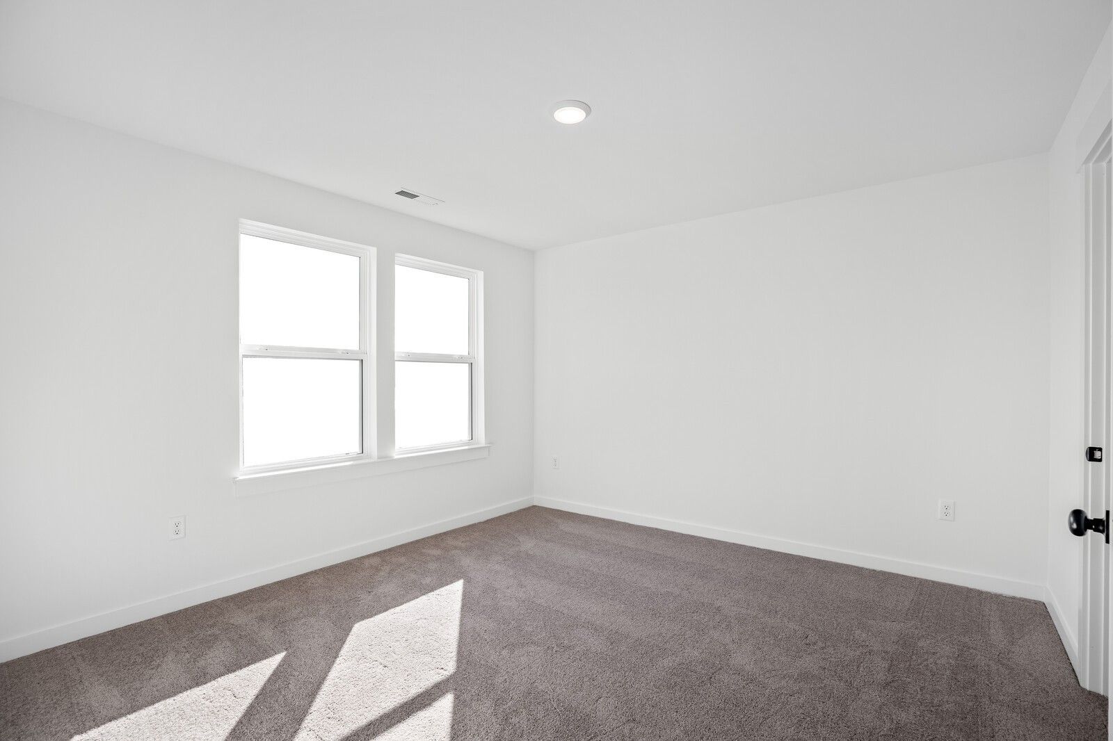 Bright empty bedroom with white walls, large sunny windows, gray carpet, and recessed lighting in Davidson Homes The Willow C, Gallatin, TN