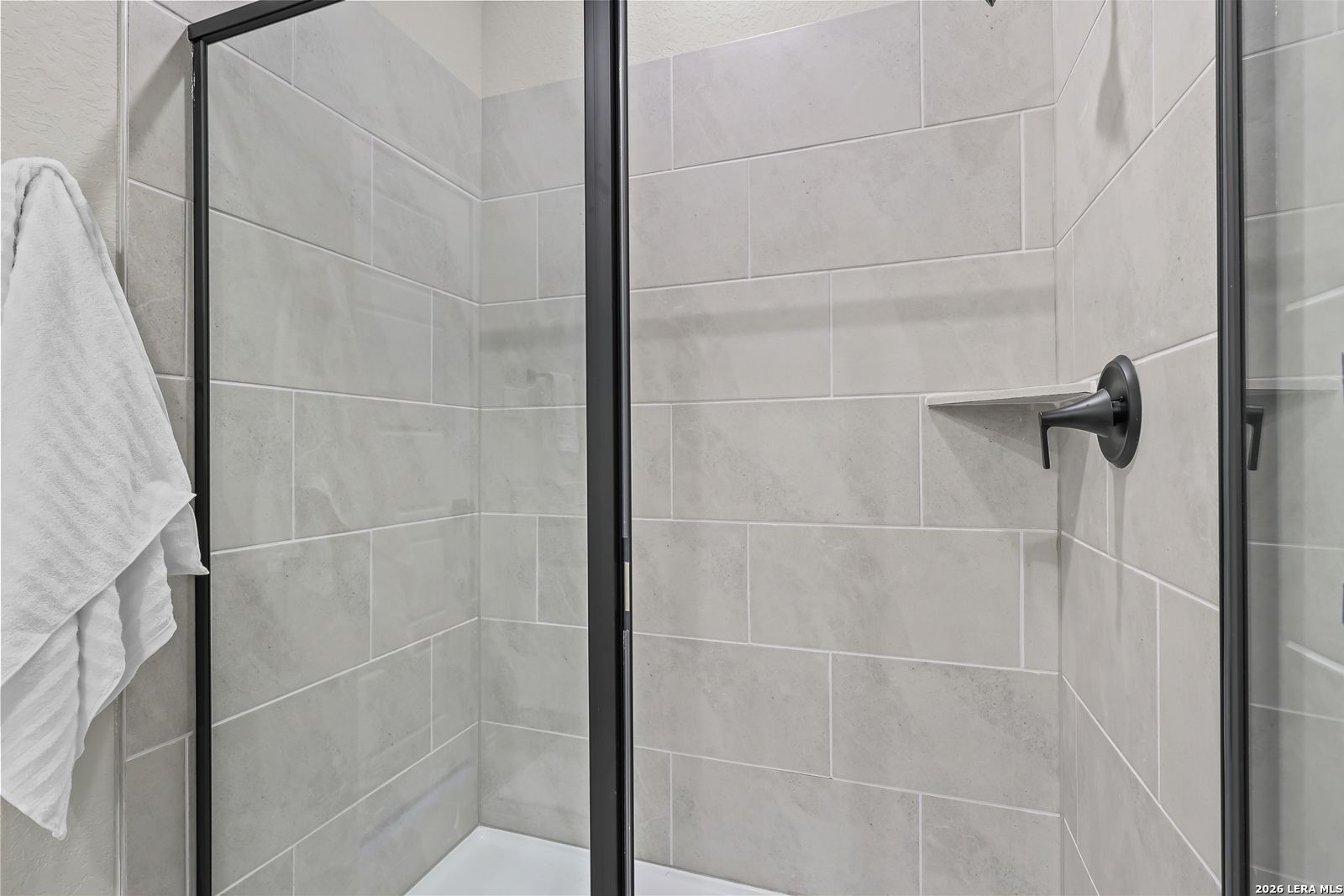 Modern walk-in shower with light gray tile and black fixtures in a Davidson Homes Daphne H floor plan in Seguin, Texas.