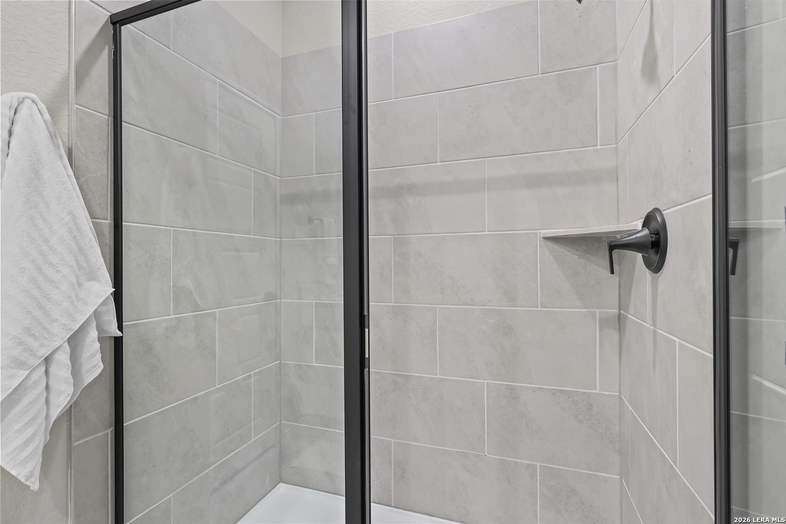 Modern walk-in shower with light gray tile and black fixtures in a Davidson Homes Daphne H floor plan in Seguin, Texas.