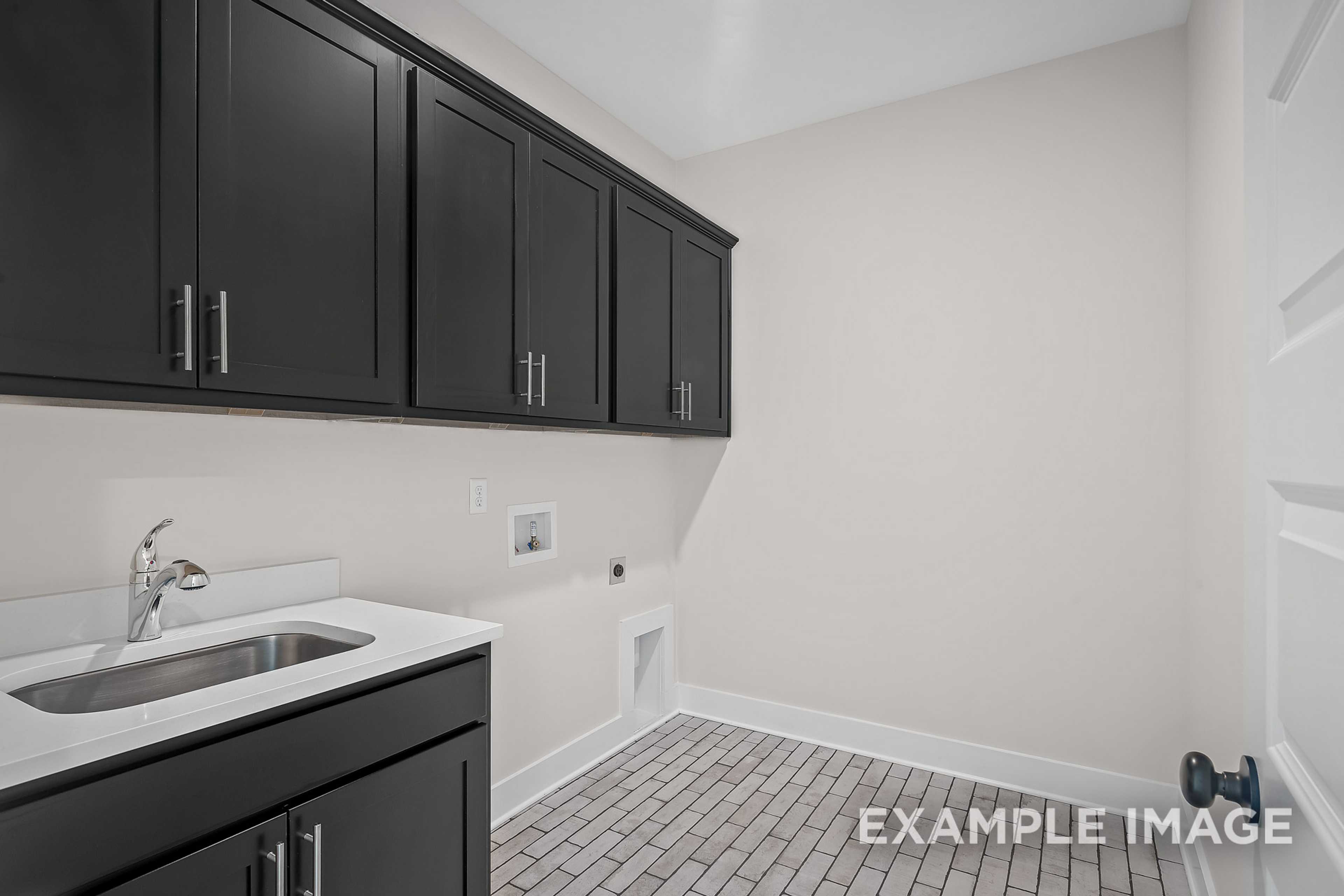 Spacious laundry room in The Hawkins with black shaker cabinets, stainless sink, and utility hookups by Davidson Homes