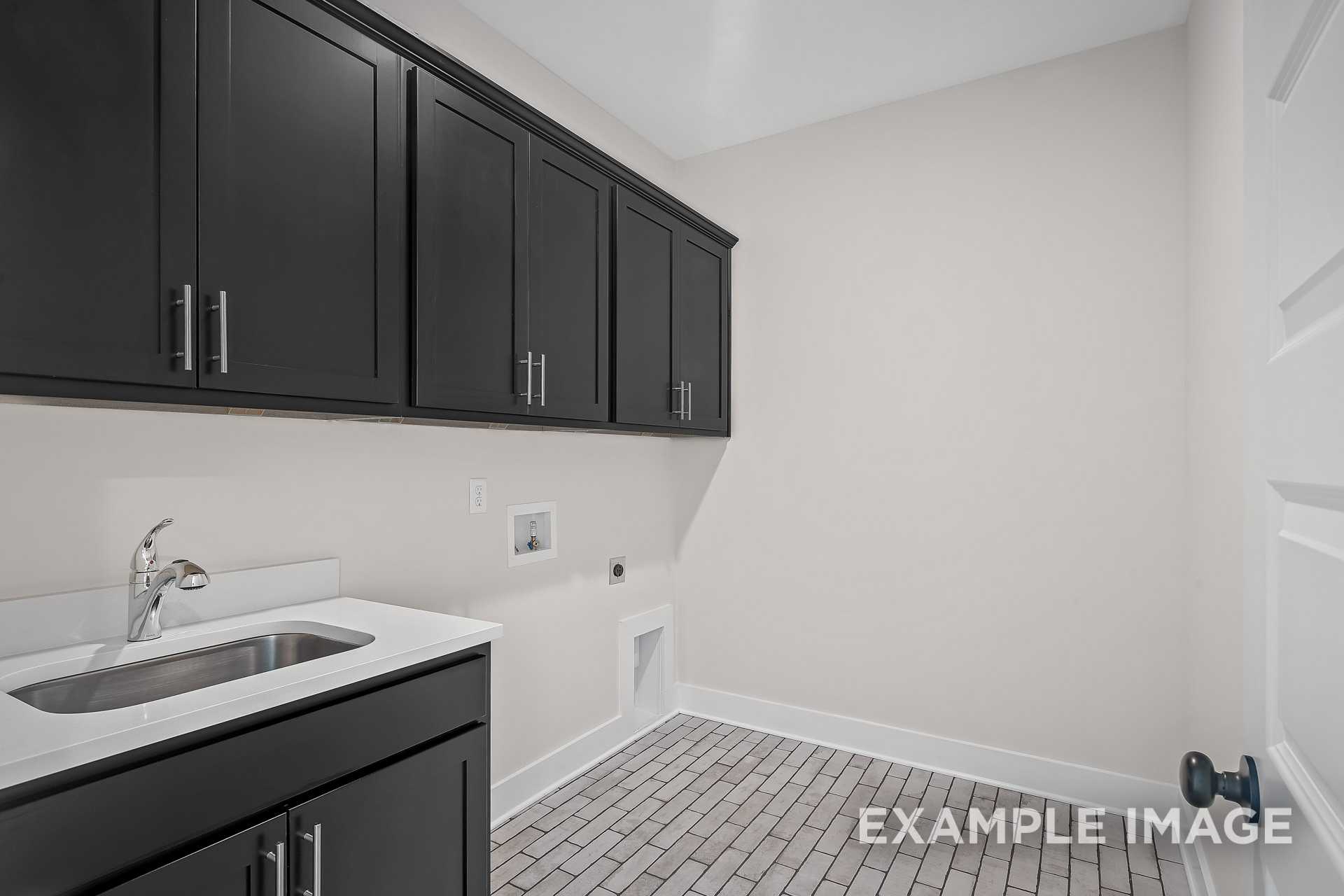 Spacious laundry room in The Hawkins with black shaker cabinets, stainless sink, and utility hookups by Davidson Homes