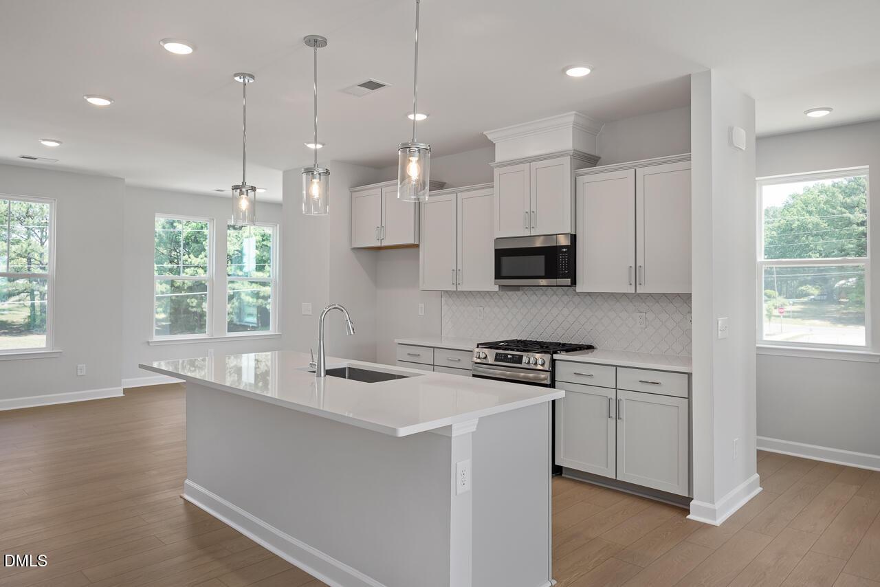 Modern kitchen with white island, light gray cabinets, and pendant lighting in The Mitchell home at Camden Park, Knightdale.