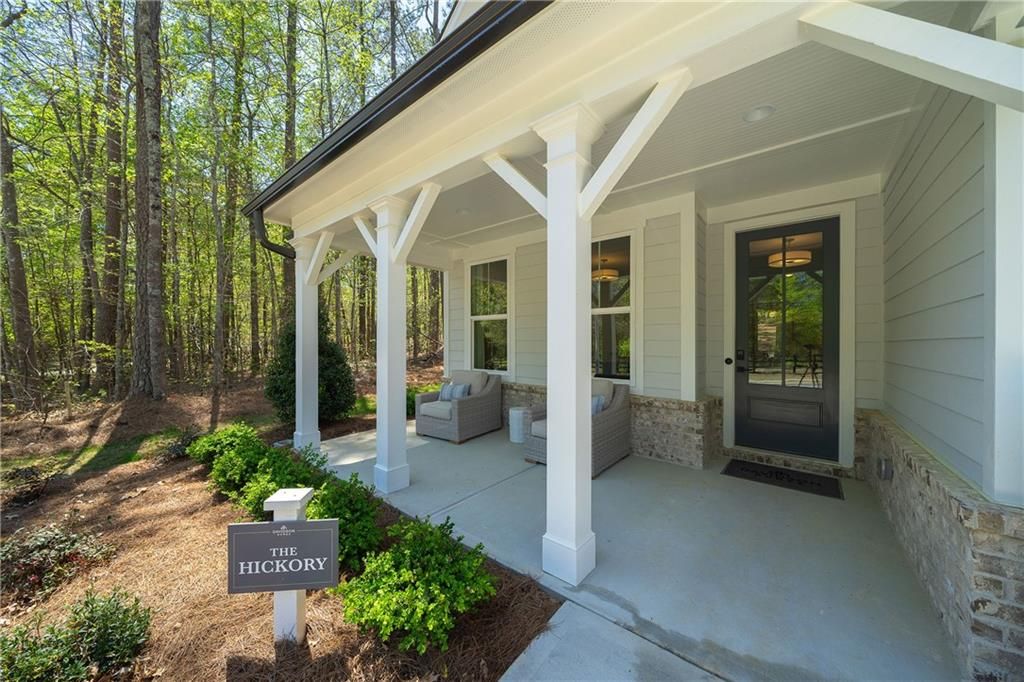 Inviting covered front porch with white columns, wicker seating, and lush trees on Davidson Homes Willow B in Riverwood, Dallas, Georgia