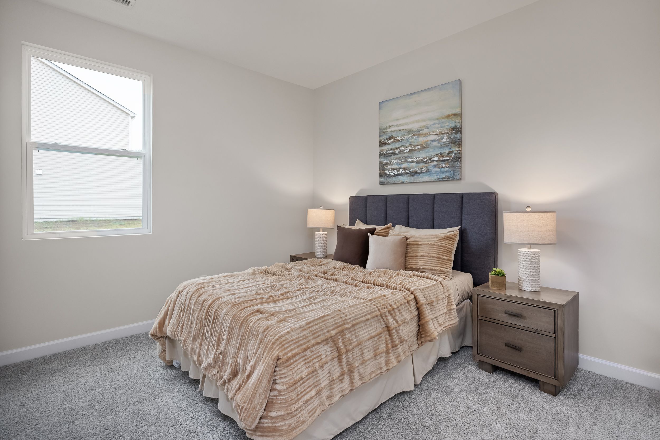 Cozy bedroom with plush tan bedding and gray upholstered headboard at Gregory Village in Lillington, NC by Davidson Homes.