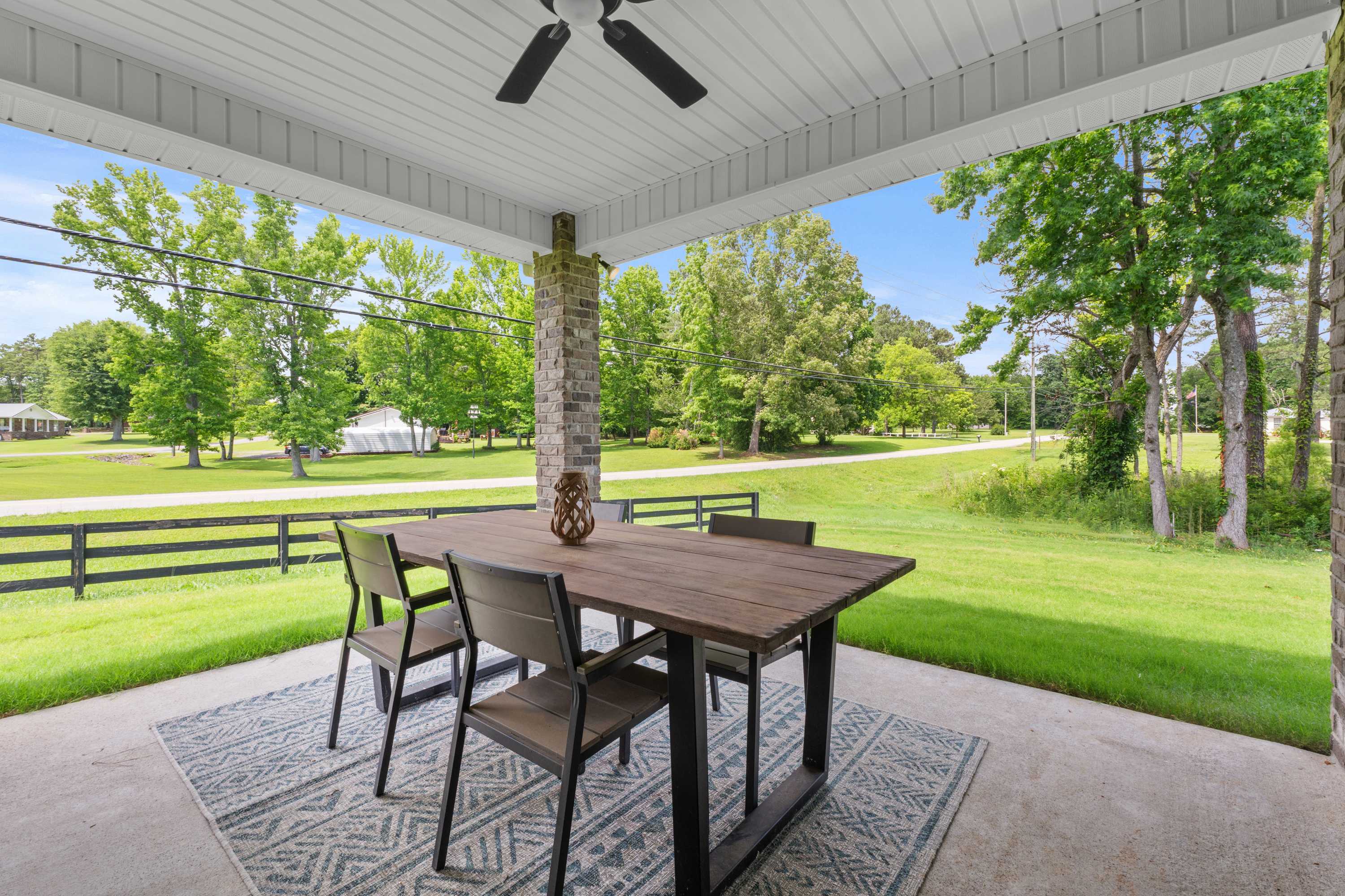Spacious covered patio at The Highlands in Arab Alabama with wooden dining table, chairs, ceiling fan and lush greenery
