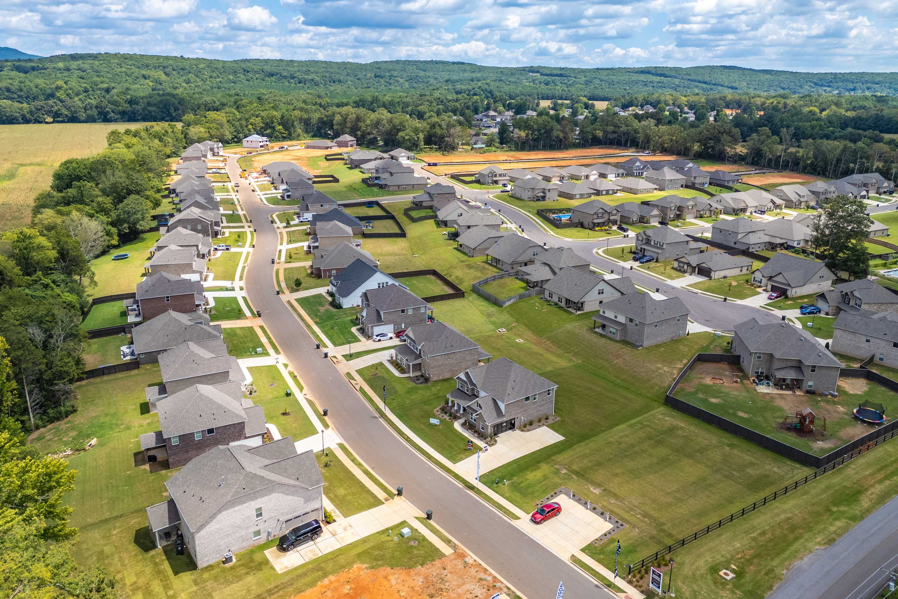 Aerial view of new single-family homes and winding streets in Creek Grove, New Market Alabama, amid woods and fields
