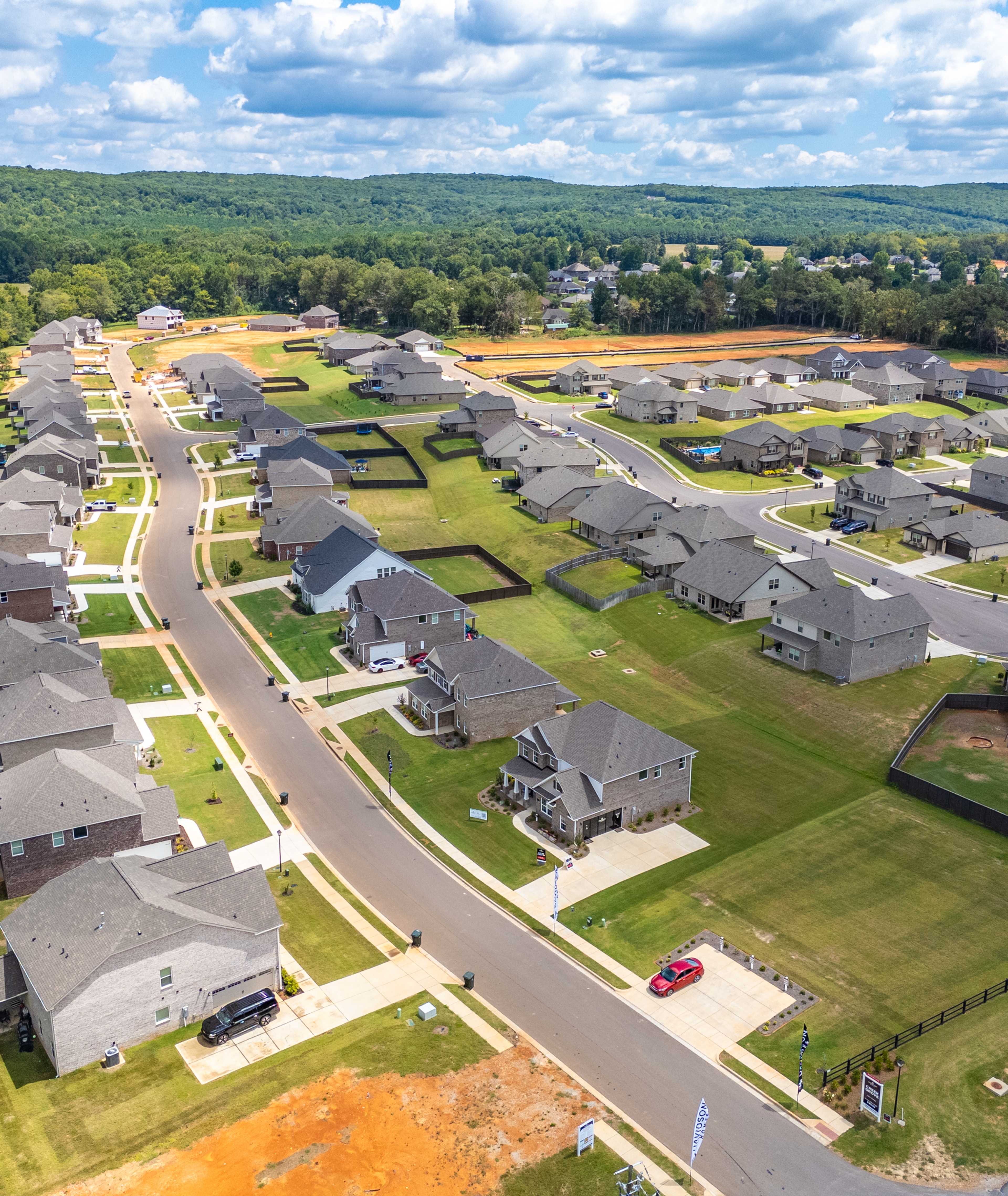 Aerial view of new homes in Creek Grove, New Market Alabama with streets, green lawns, woods, and construction areas