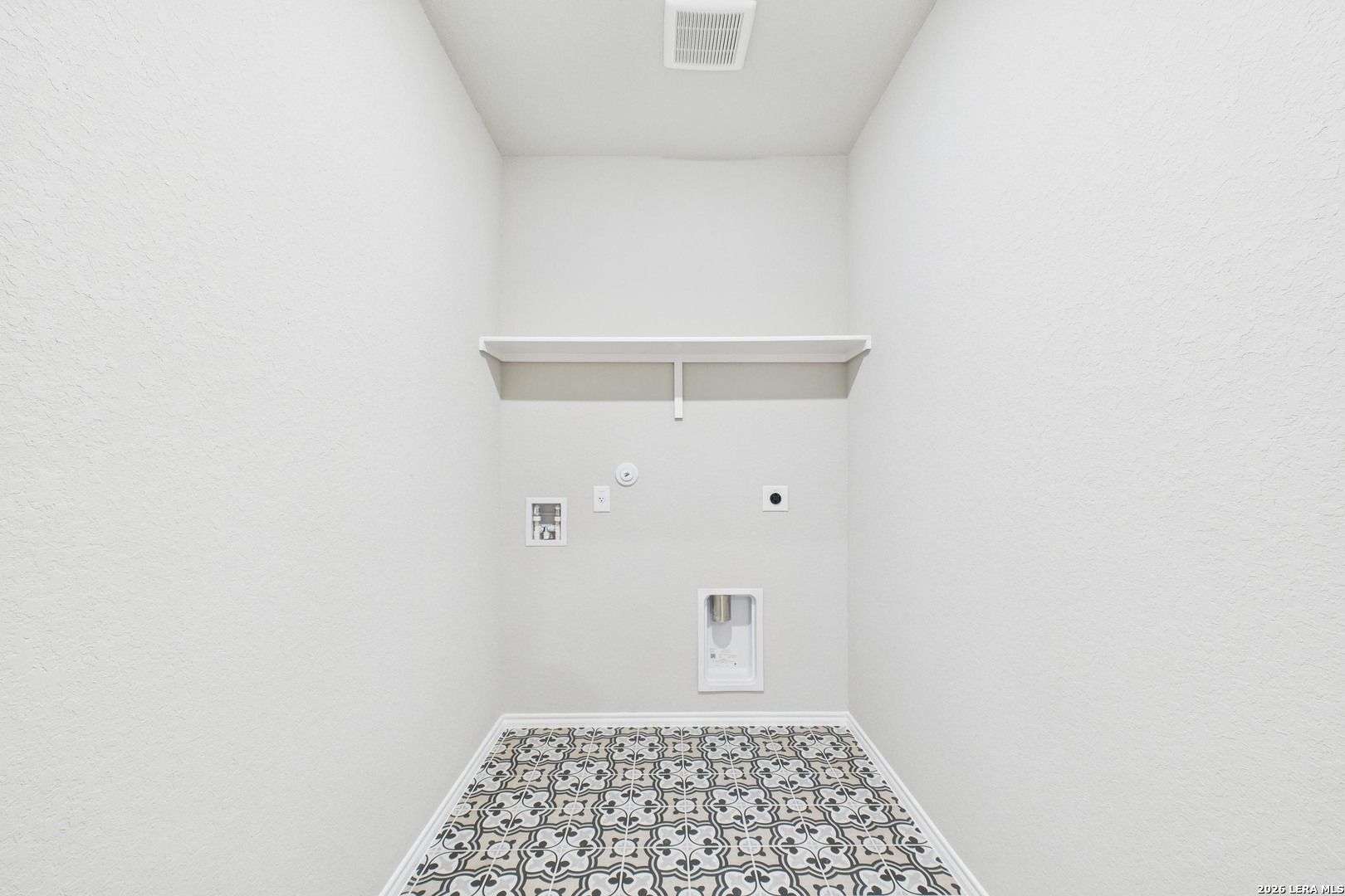 Spacious laundry room with utility sink, washer-dryer hookups, shelves, and patterned tile floor in Davidson Homes The Douglas E, Bricewood, San Antonio