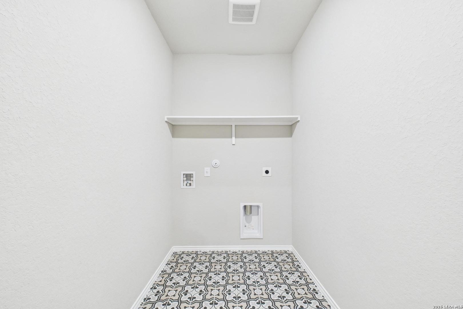 Spacious laundry room with utility sink, washer-dryer hookups, shelves, and patterned tile floor in Davidson Homes The Douglas E, Bricewood, San Antonio