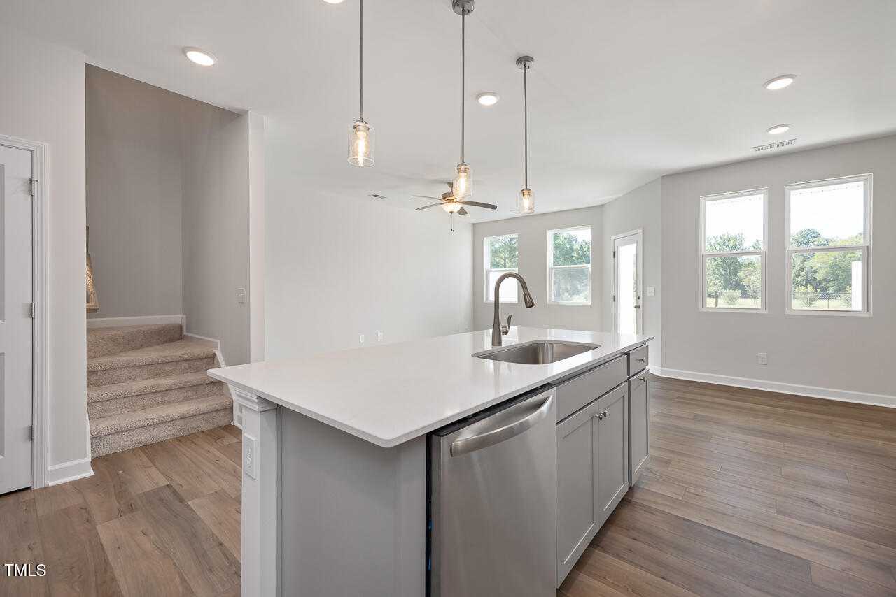 Bright modern kitchen with white quartz island, pendant lights, stainless sink, and open layout in Davidson Homes The Graham, Fuquay-Varina, NC