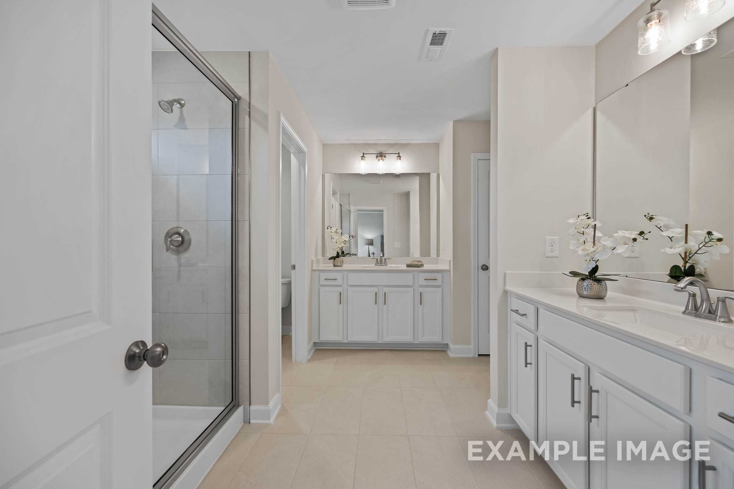 Spacious master bathroom in The Preston B featuring frameless glass shower, double vanity with orchids, and neutral tones