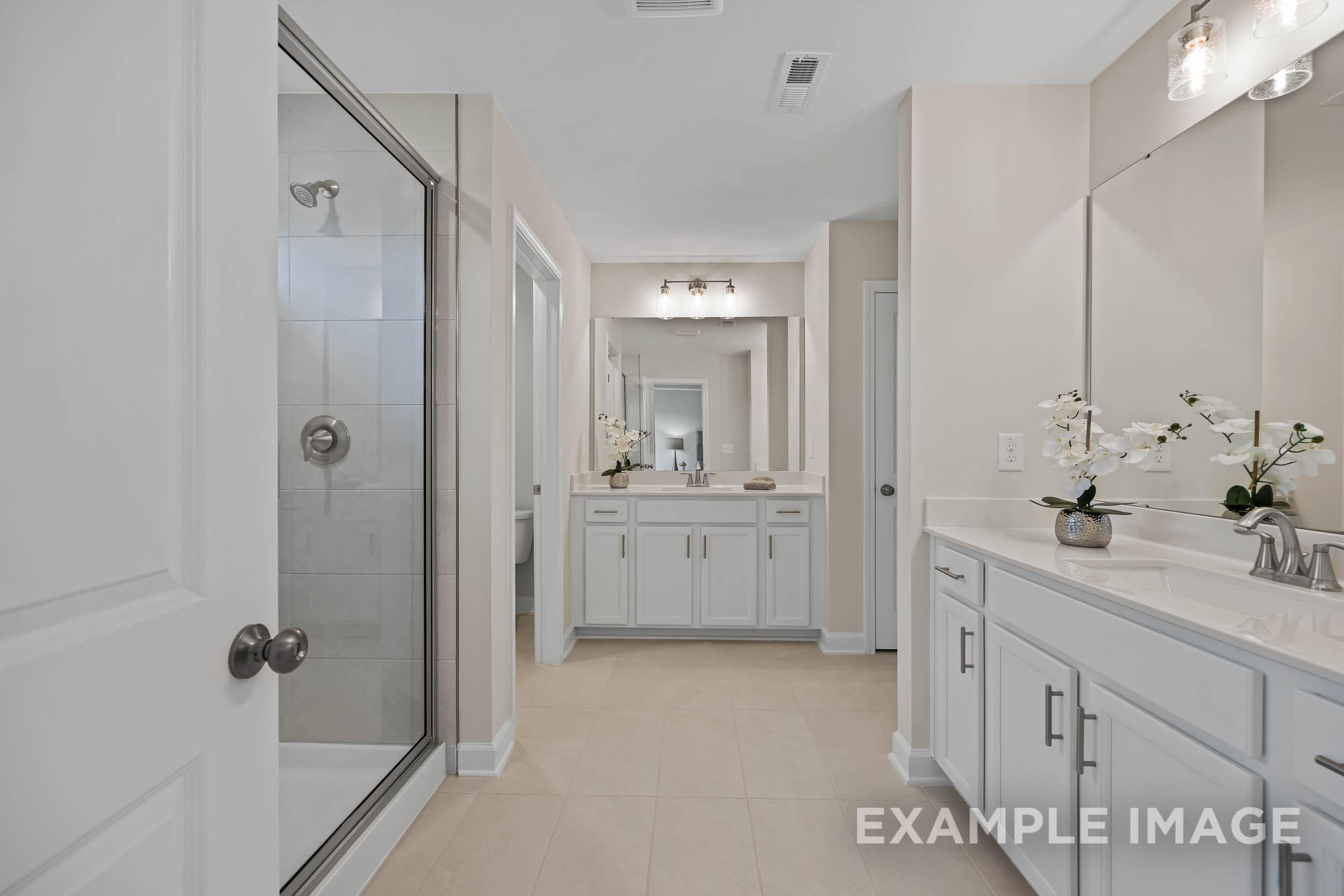 Spacious master bathroom in The Preston B featuring frameless glass shower, double vanity with orchids, and neutral tones