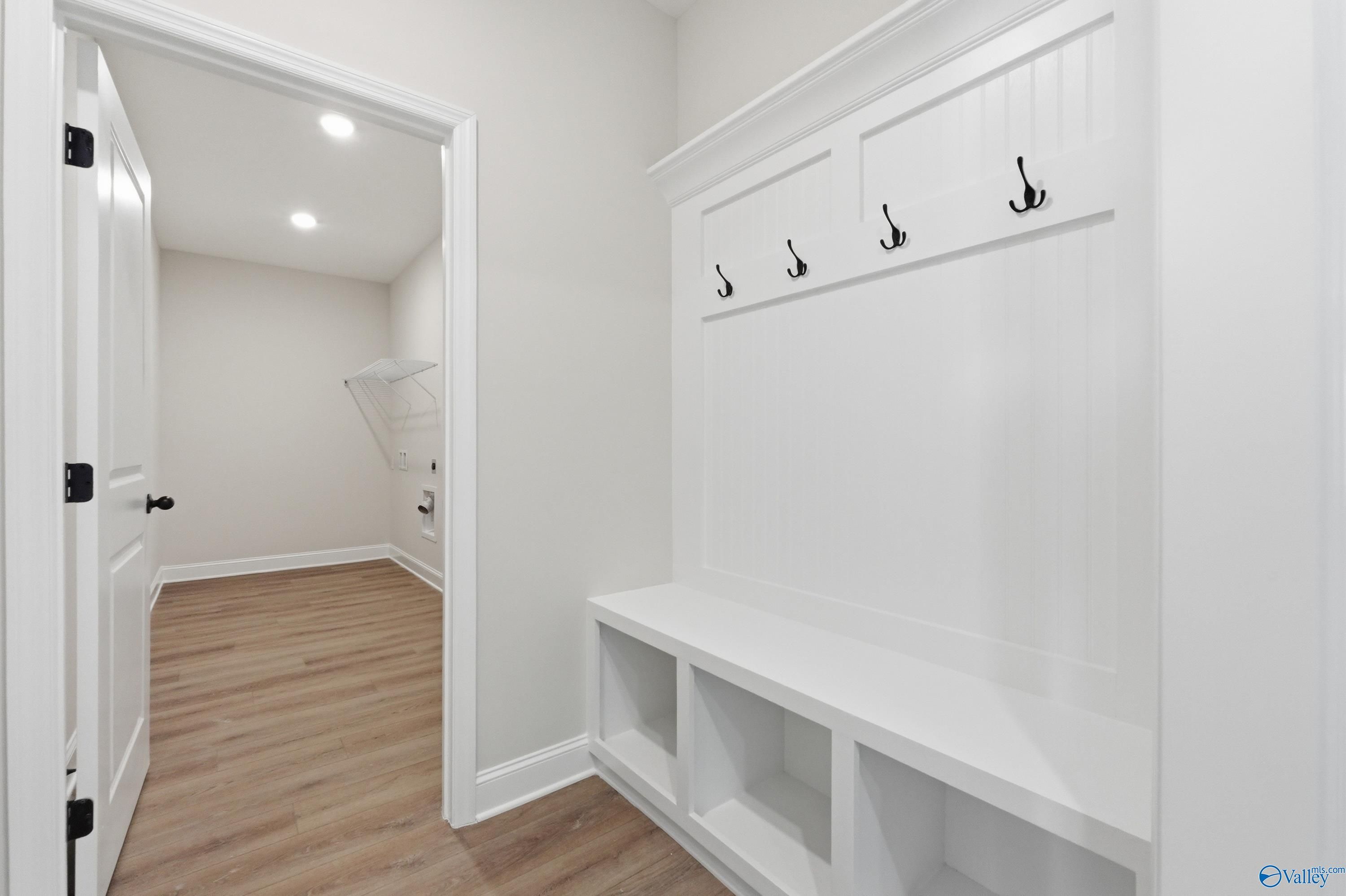 White built-in mudroom bench with coat hooks, cubbies, and adjacent laundry in Davidson Homes The Rockford B, Athens, Alabama