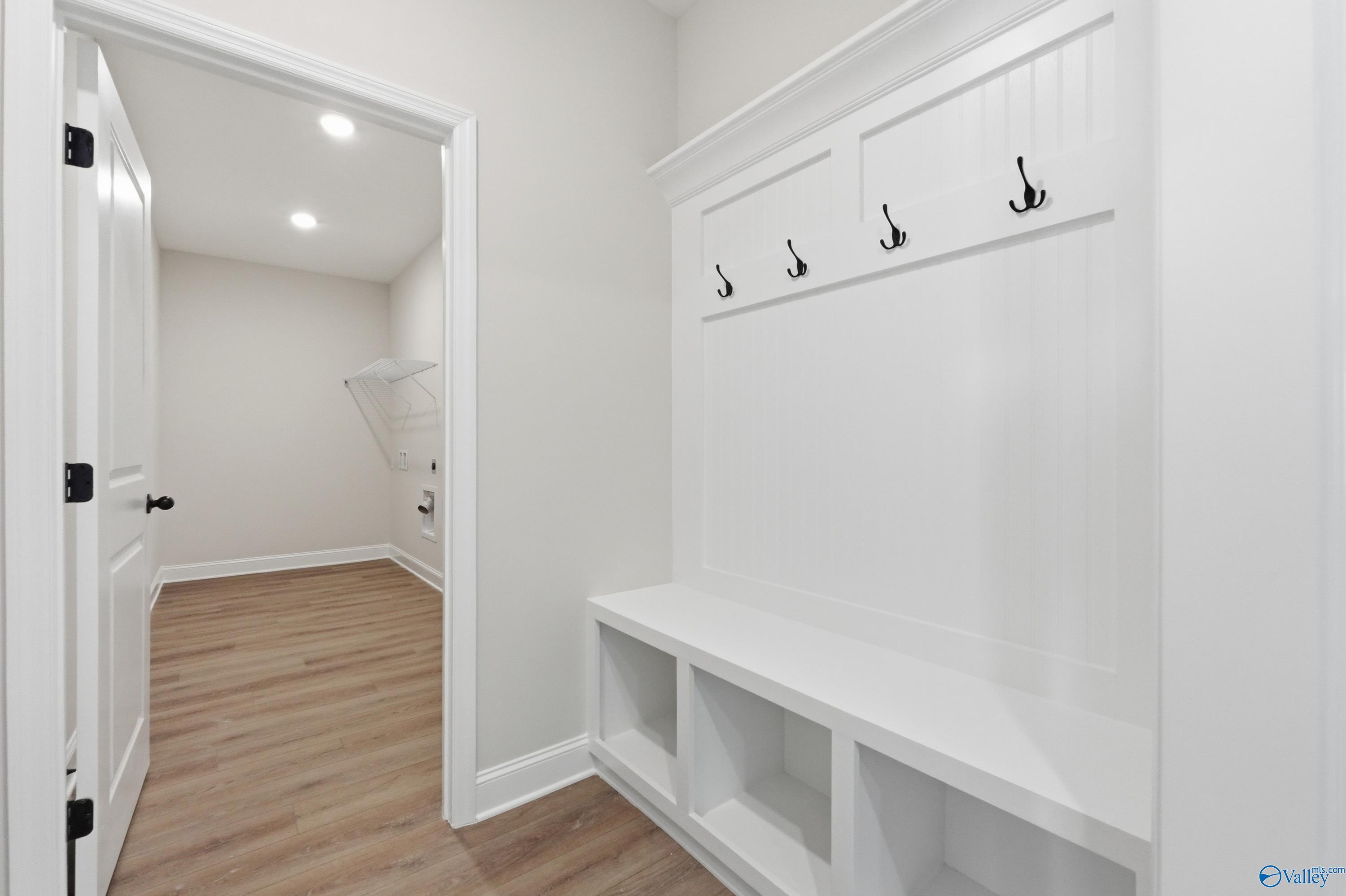 White built-in mudroom bench with coat hooks, cubbies, and adjacent laundry in Davidson Homes The Rockford B, Athens, Alabama